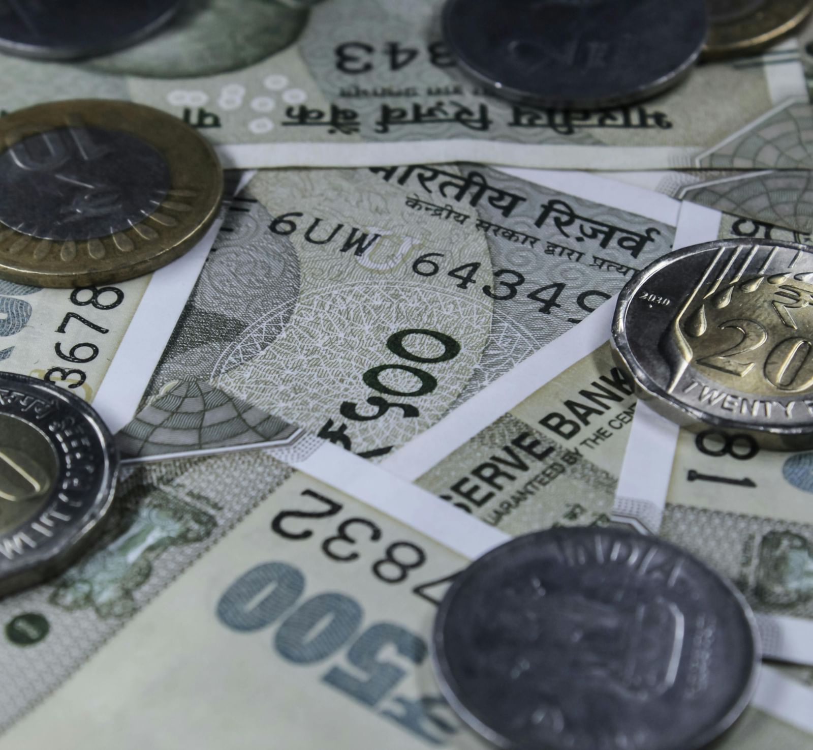 A close-up shot of several Indian currency notes of five hundred rupee denomination along with several coins.