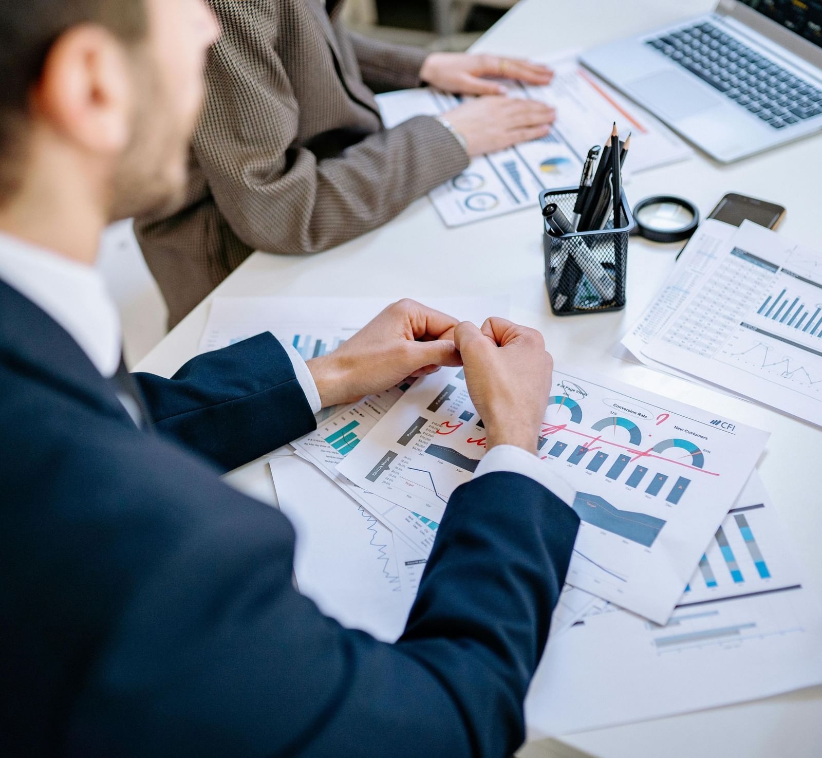 A person dressed in business formals in front of a table with sheets full of data scattered over it.