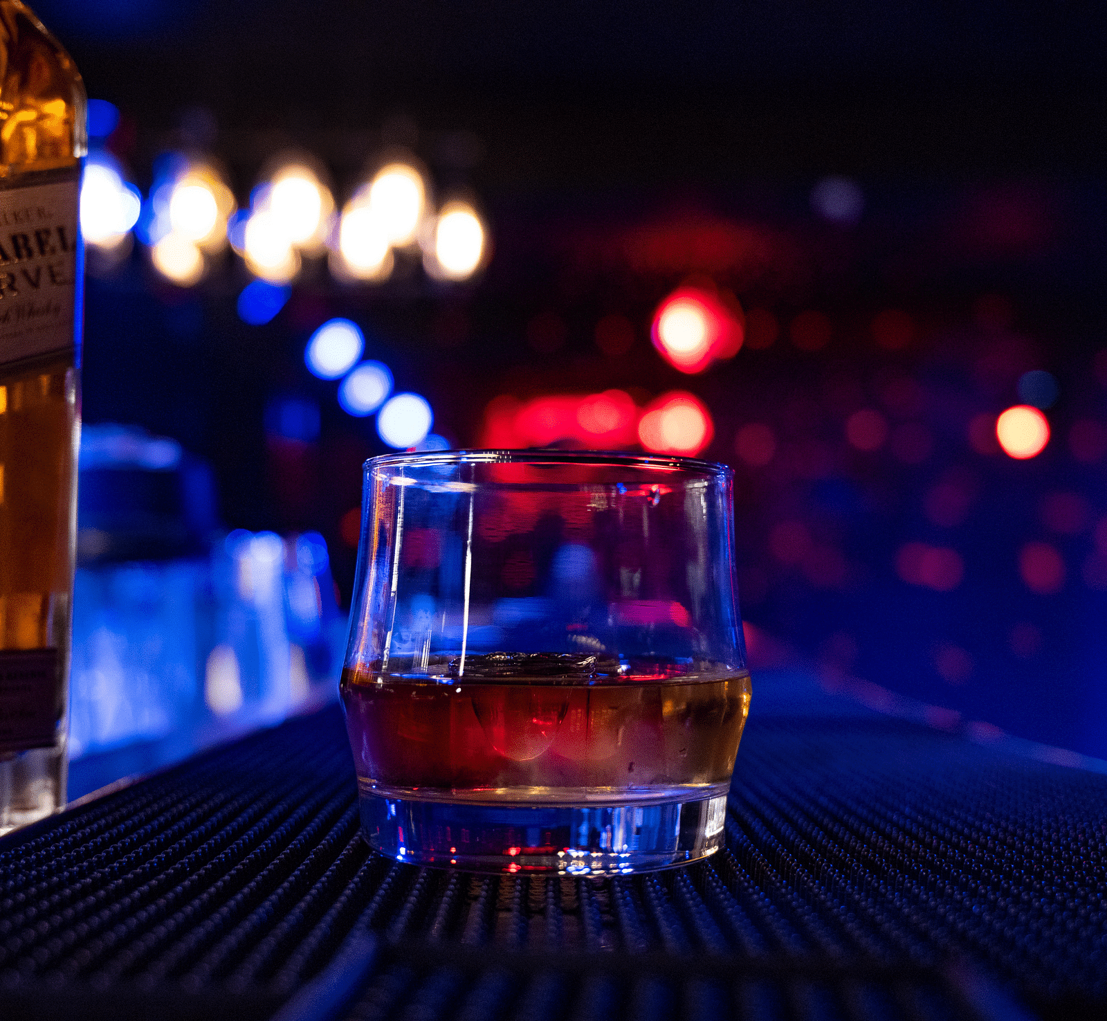 a close up image of a glass holding whisky in a dimly lit bar counter at the bourbon club and lounge - The Tattva Boutique Resort