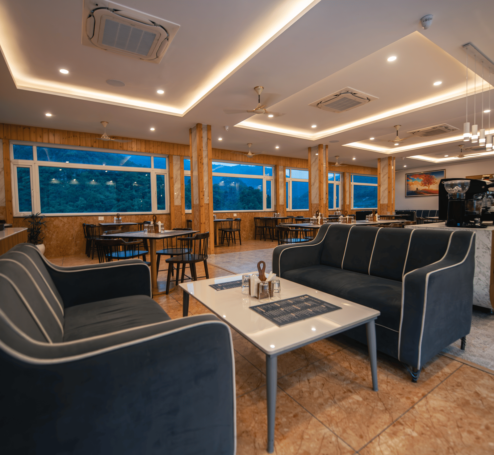 A restaurant at The Tattva Devaprayag with dark grey couches and a coffee table.