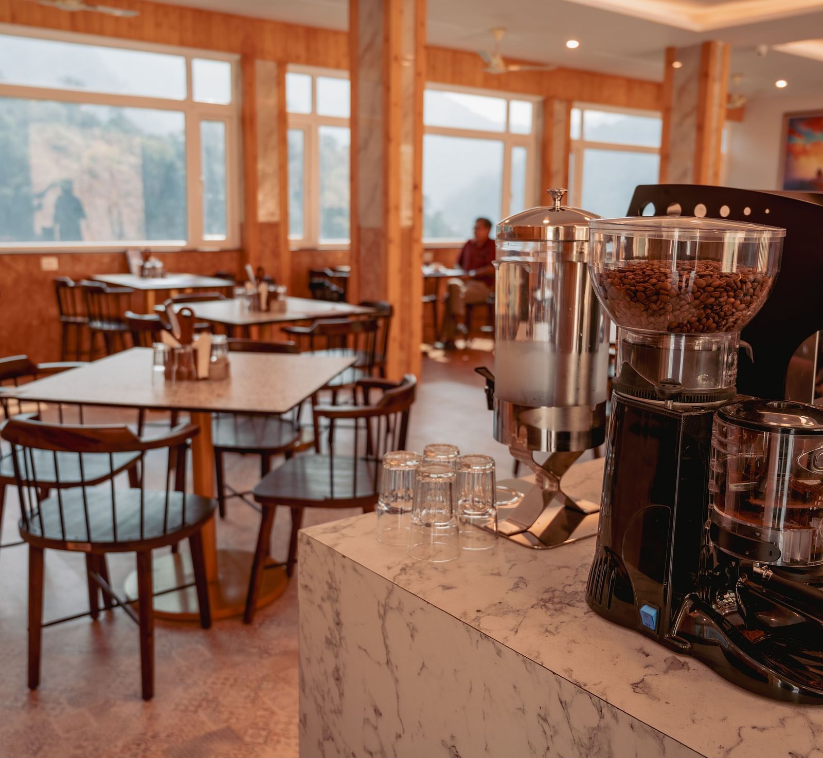 Image of the in-house restaurant featuring a fine dining setup, natural lights and a coffee machine | The Tattva Devprayag