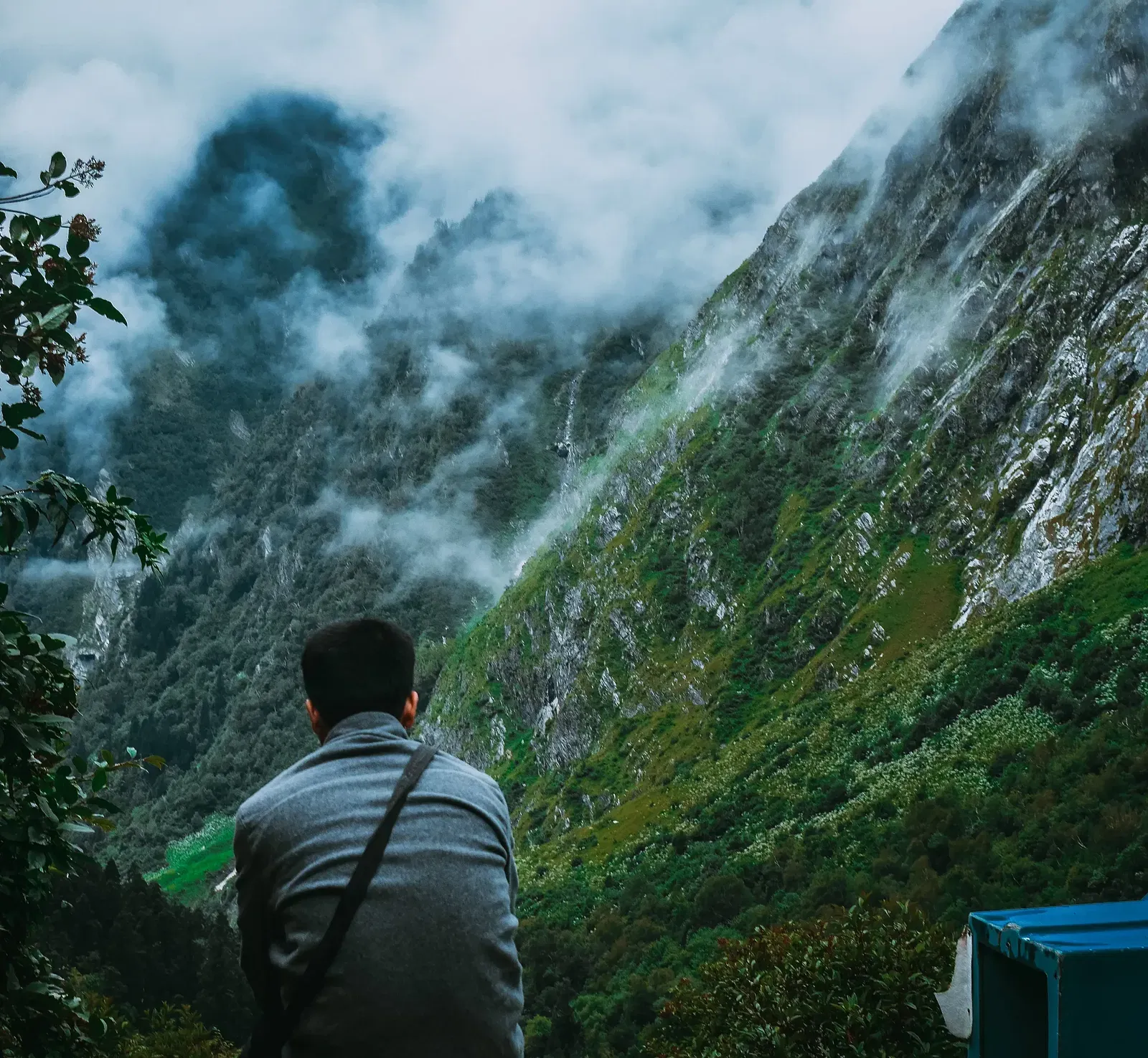 A man sits with his back to the viewer, facing a misty mountain valley landscape, with a tent visible in the foreground.
