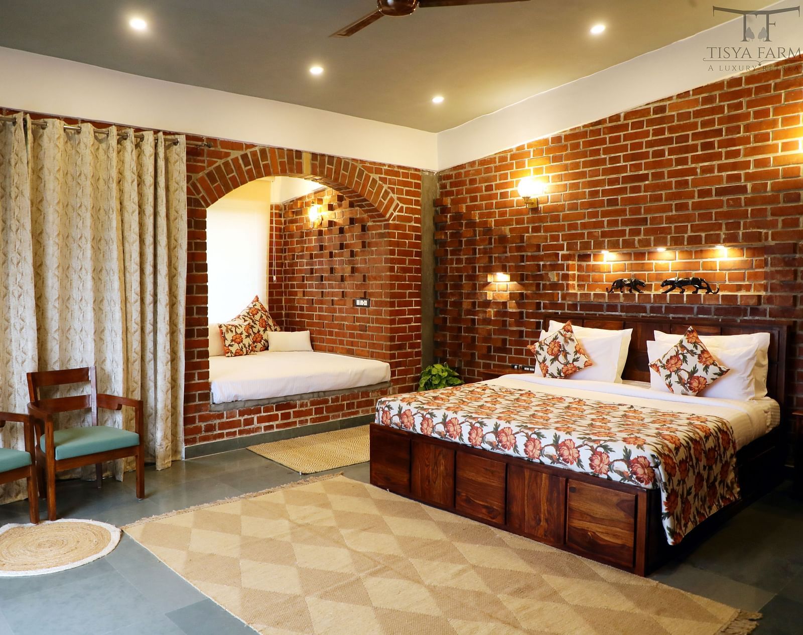 A bedroom at Tisya Farms, Gurgaon with a double bed, chairs, brick walls, curtains, and overhead lighting.