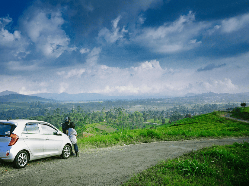 A car parked on a scenic hillside road with lush greenery and mountains of Parasnath, Dhanbad.