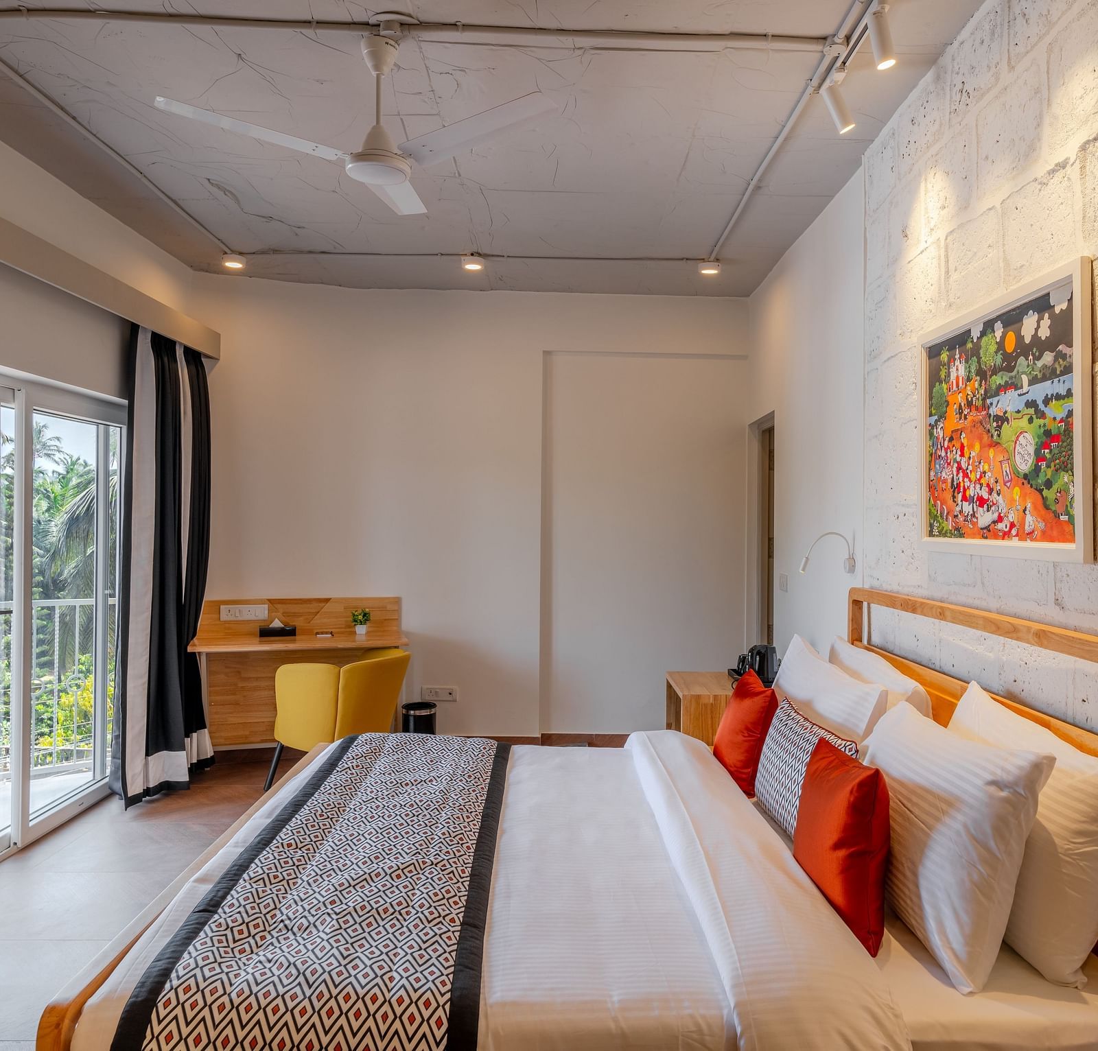 Bright hotel room with, flat TV screen, work desk and chair, vibrant art on the wall, and an access to the balcony at Bedzzz Xclusiv Morjim, Goa