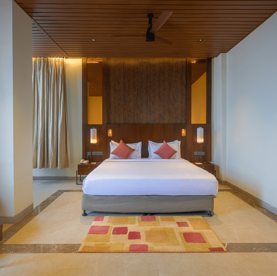 Hotel bedroom with a king size bed, patterned rug, wooden ceiling, bedside tables and warm ambient lighting.