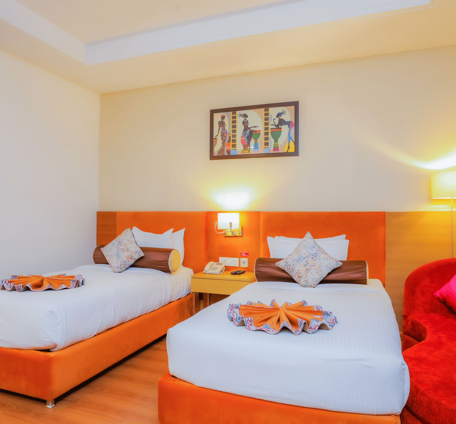 A forefront angle of a twin bedroom, showing two beds with orange and red accents at The Conway, Meerut.