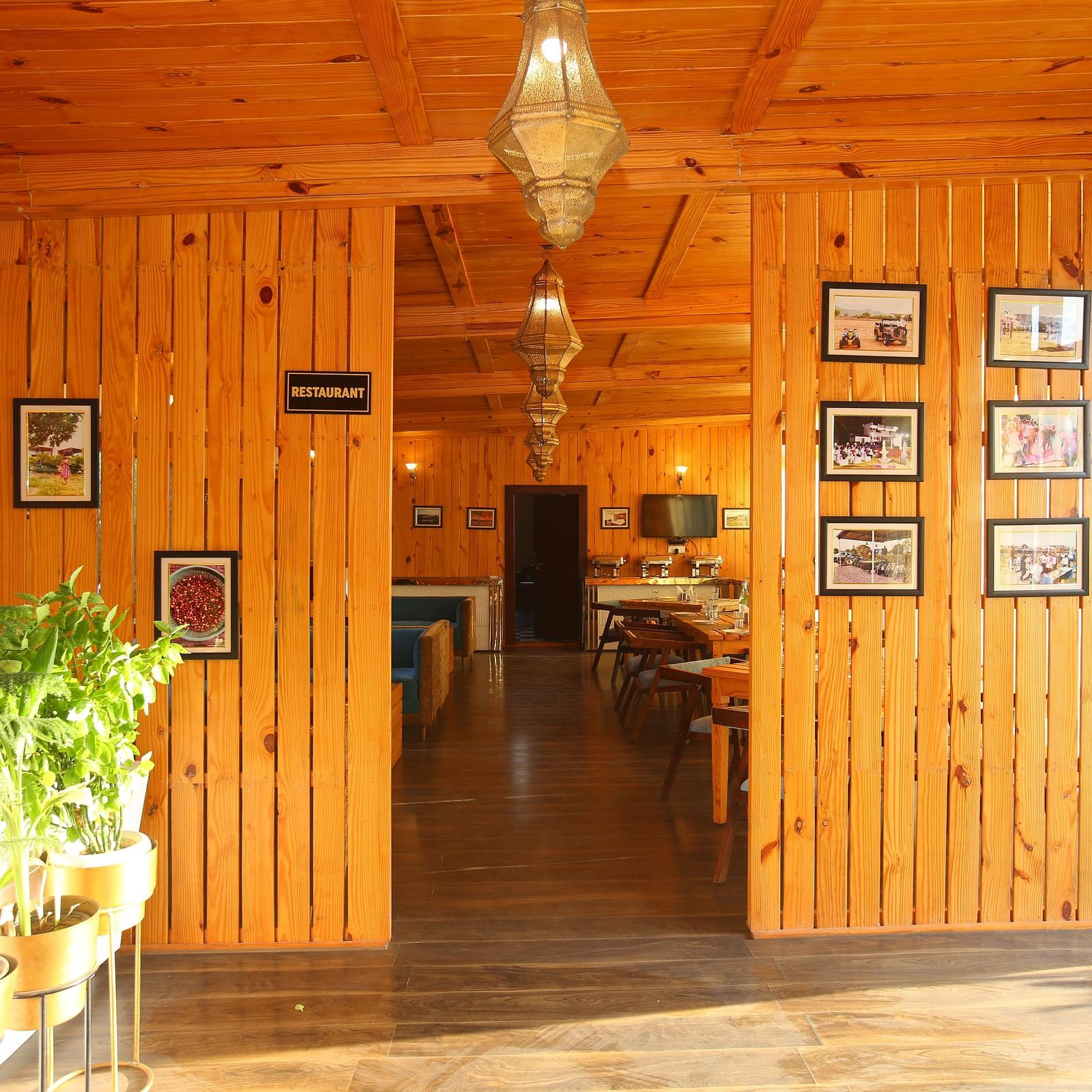 Entryway to the dining area featuring wall-mounted photo frames, a hanging lamp, and potted plants on the side at Aanandam Resort & Spa