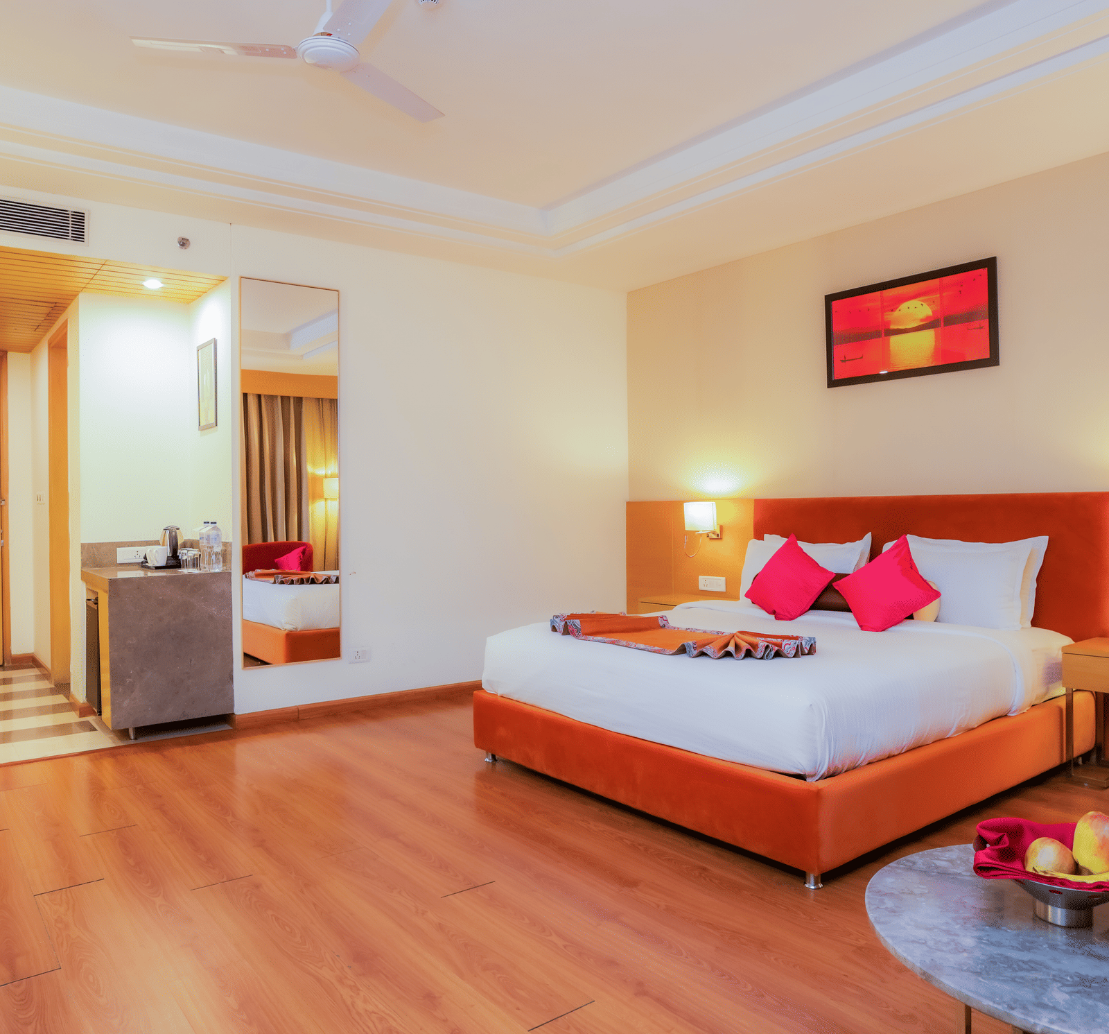 A welcoming hotel room showing the bed, a fruit bowl, and a luggage trolley near the entrance at The Conway, Meerut.