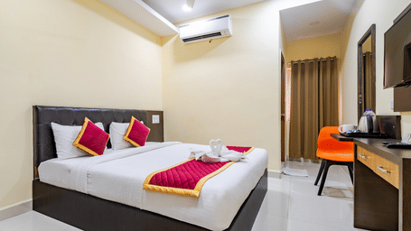 A bedroom at Lemonridge by Monday Hotels - Kukatpally is furnished with a large bed, an orange chair by a small desk, curtains, ceiling fan, and an A/C.
