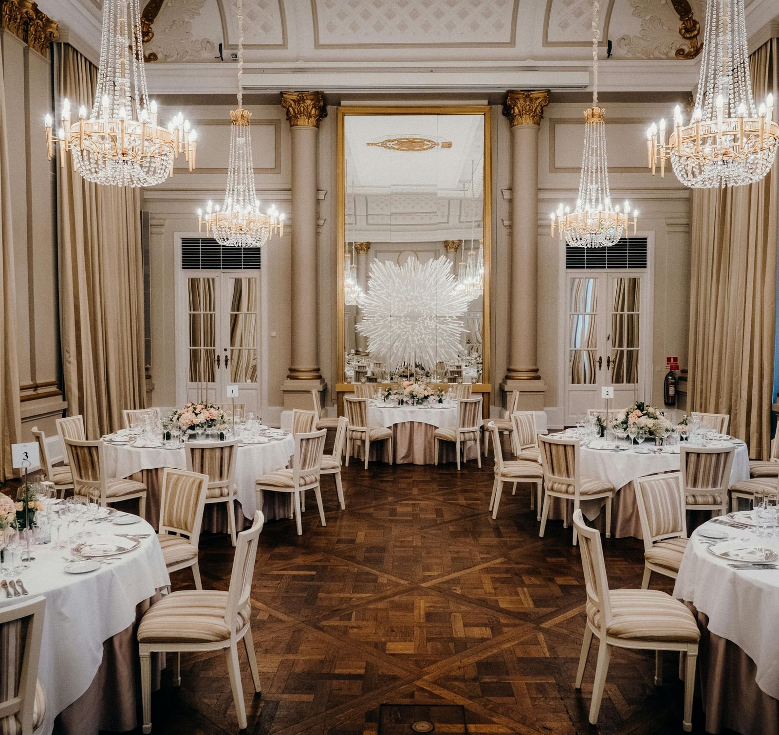 A grand ballroom featuring multiple round tables with linens and warm lighting
