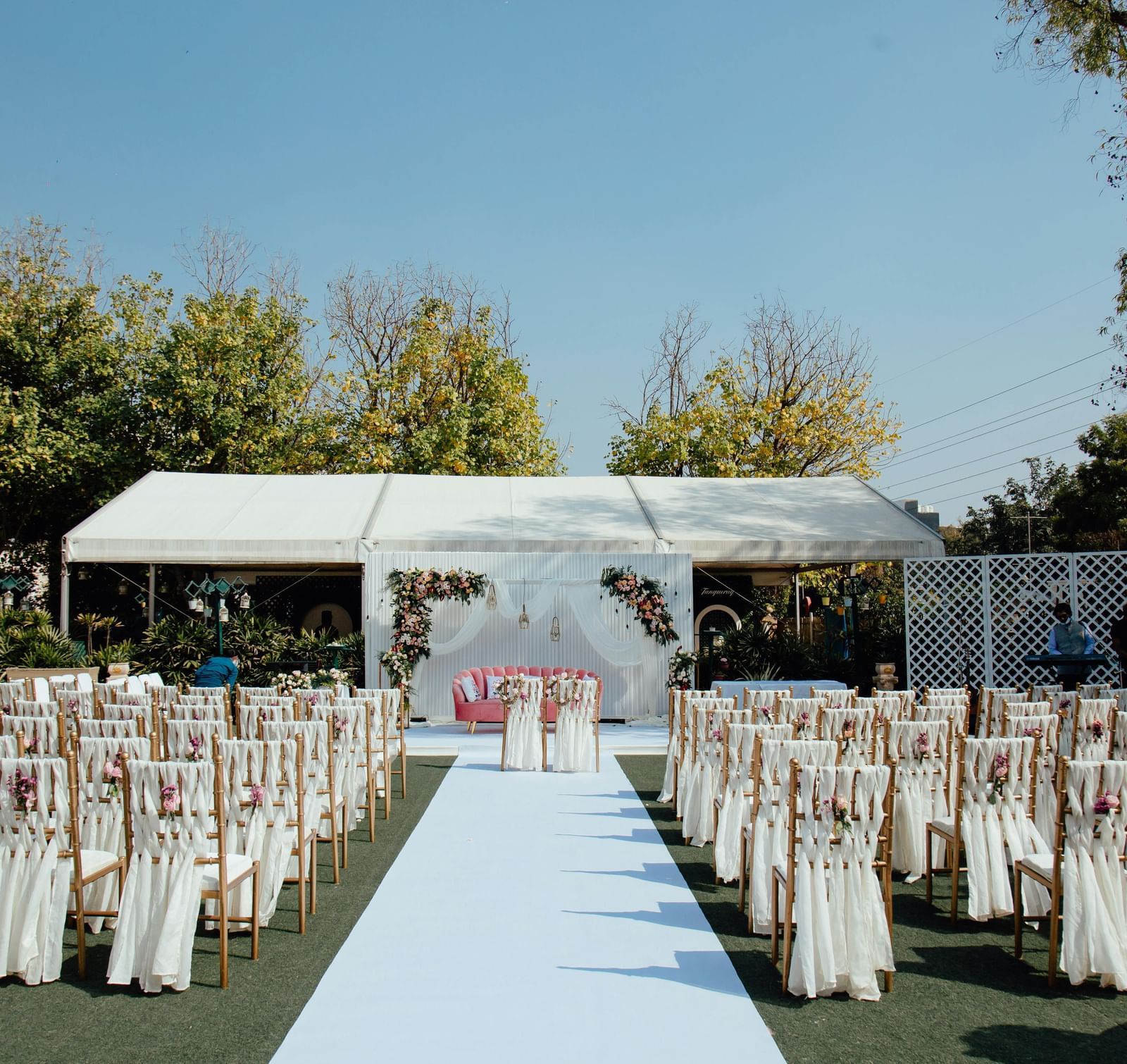 Wedding aisle with chairs and a stage under a canopy in an open lawn.
