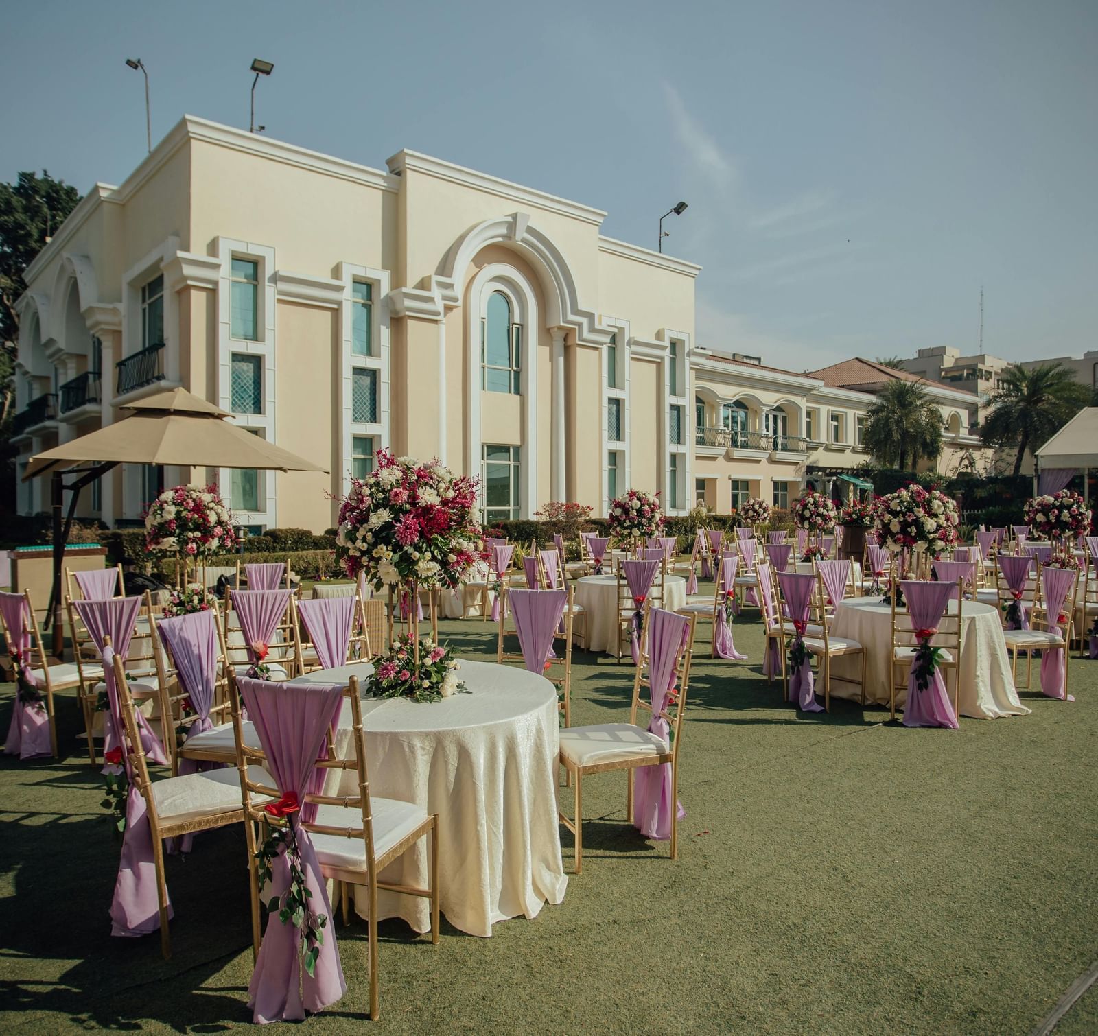 Outdoor wedding setup with round tables, floral decor, and a building in the background.