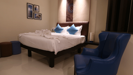 A cosy corner of a guest room featuring a high-back blue armchair and colourful round ottomans at The Bull Boutique Hotel.