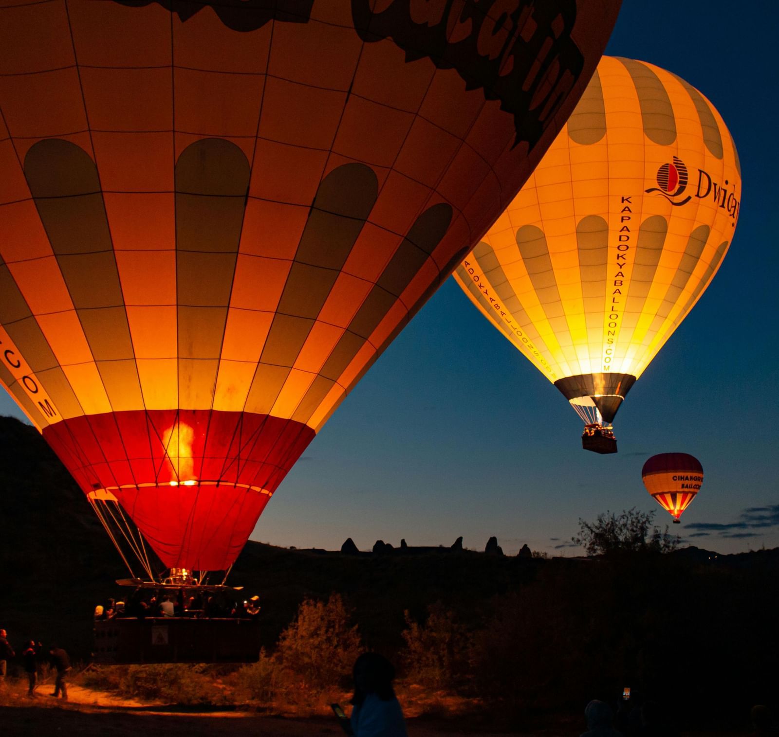 A close-up shot of a hot air balloon lifting off the ground during the late evening hours featuring the golden halo emitting from the balloons floating in the air.
