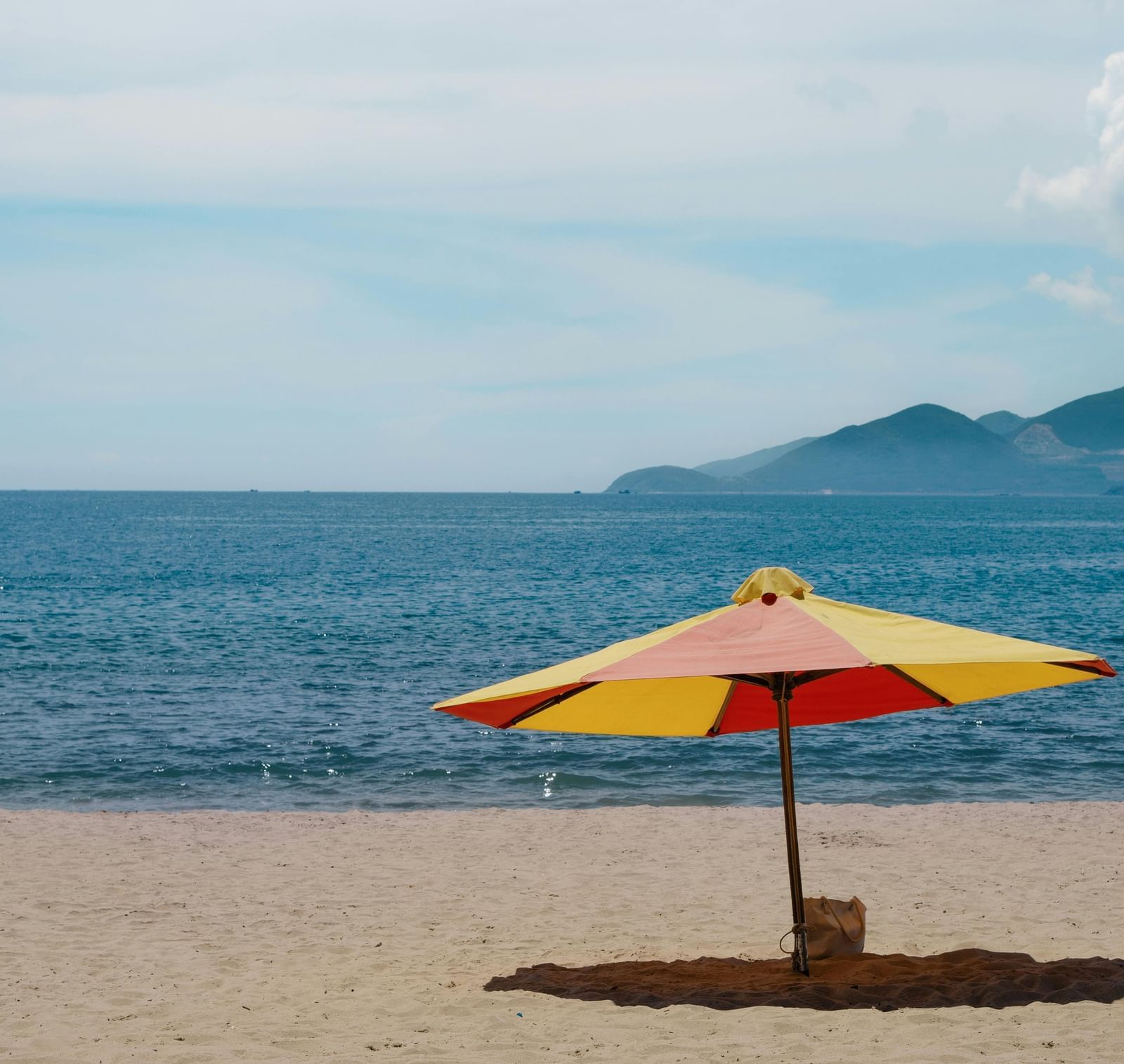 An umbrella kept on an empty beach with a calm sea in front of it.