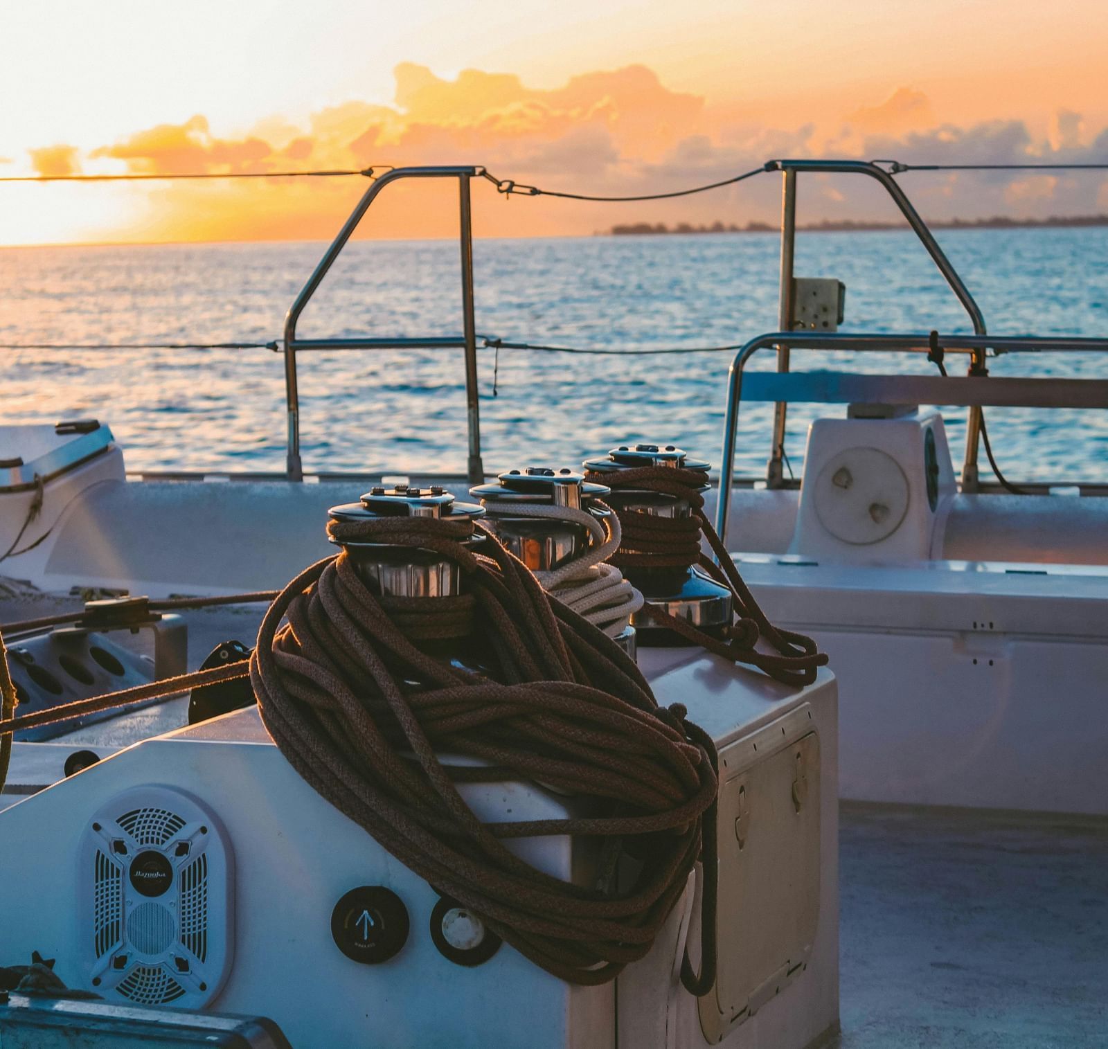The dock area of a yacht overlooking the beautiful cloudy skies with orange hues over the ocean.