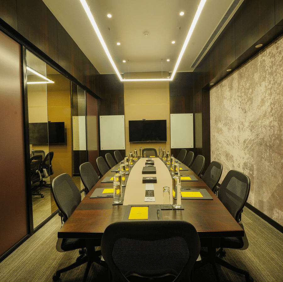 A modern conference room with long wooden table, black chairs, notepads, and wall-mounted screen