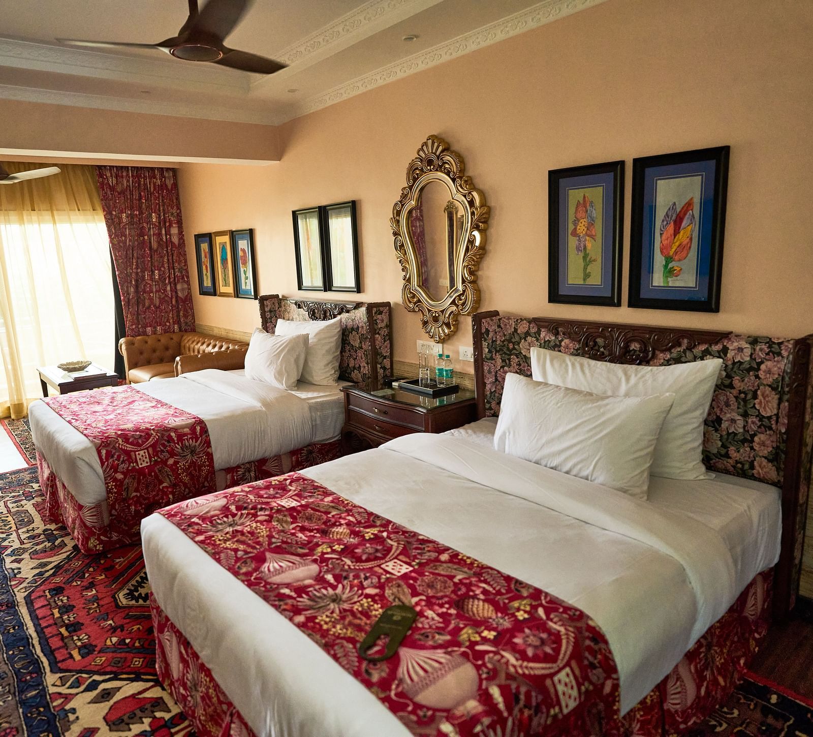 Side view of a spacious room featuring a double bed, wall-mounted frames for decoration, and windows elegantly covered with curtains at Mayfair Manor, Alibag