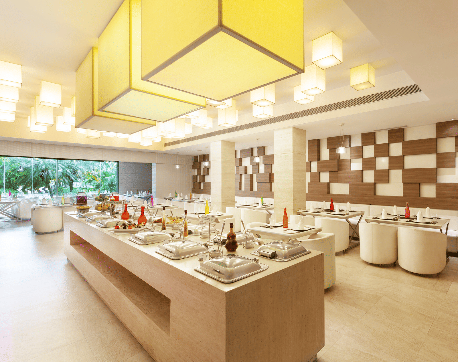 A diagonal view of a restaurant with an island in the middle featuring buffet items, surrounded by tables and chairs on the sides | Cenneys Gateway