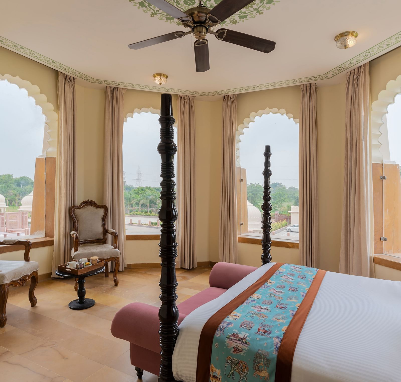 Elegant bedroom with arched windows overlooking scenic landscape at Kesar Bagh Palace.