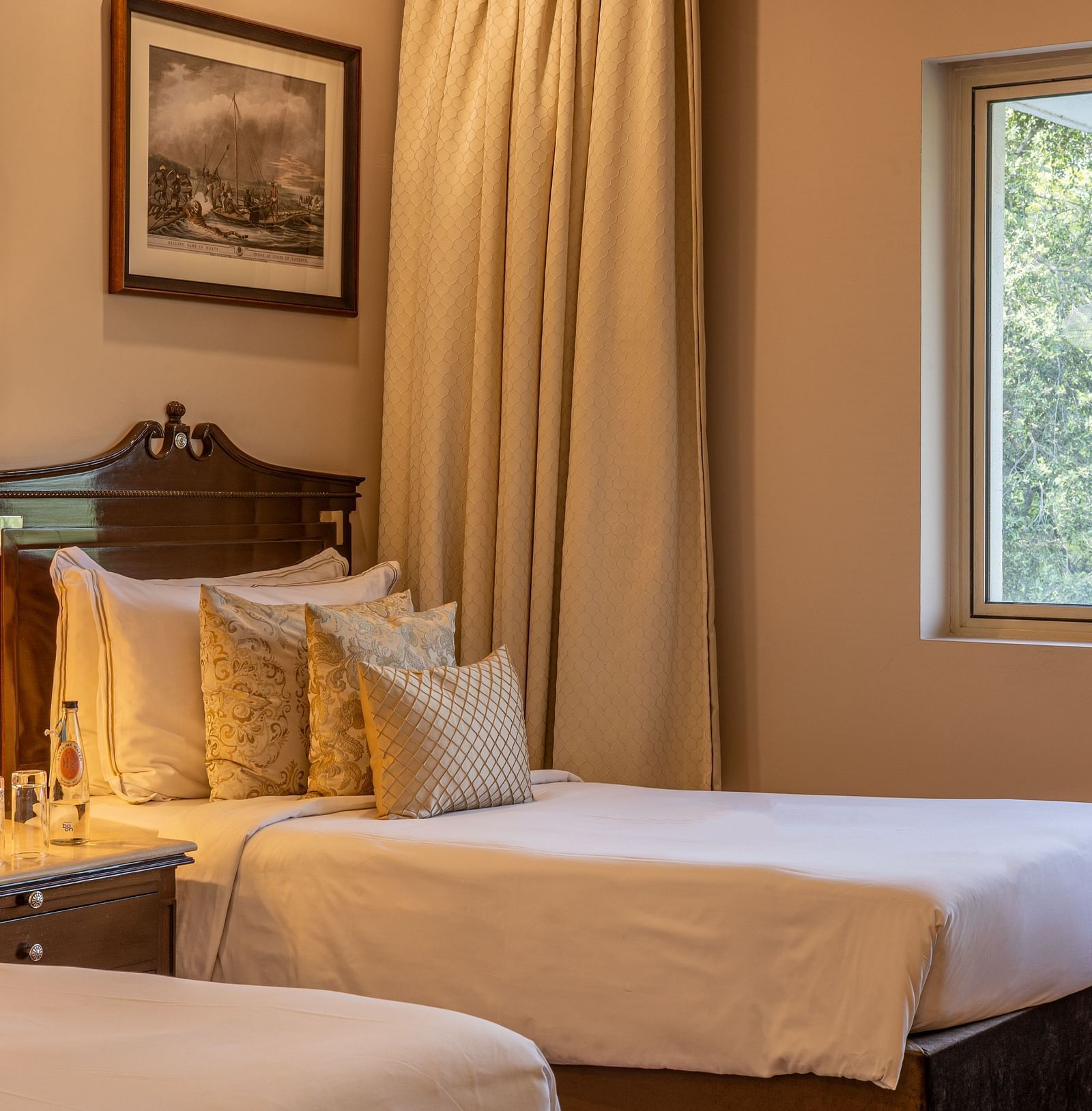 Grand Luxury Twin Bed Room at The Claridges New Delhi, featuring elegant twin beds, framed photos on the wall, a bedside lamp between the beds, and a window