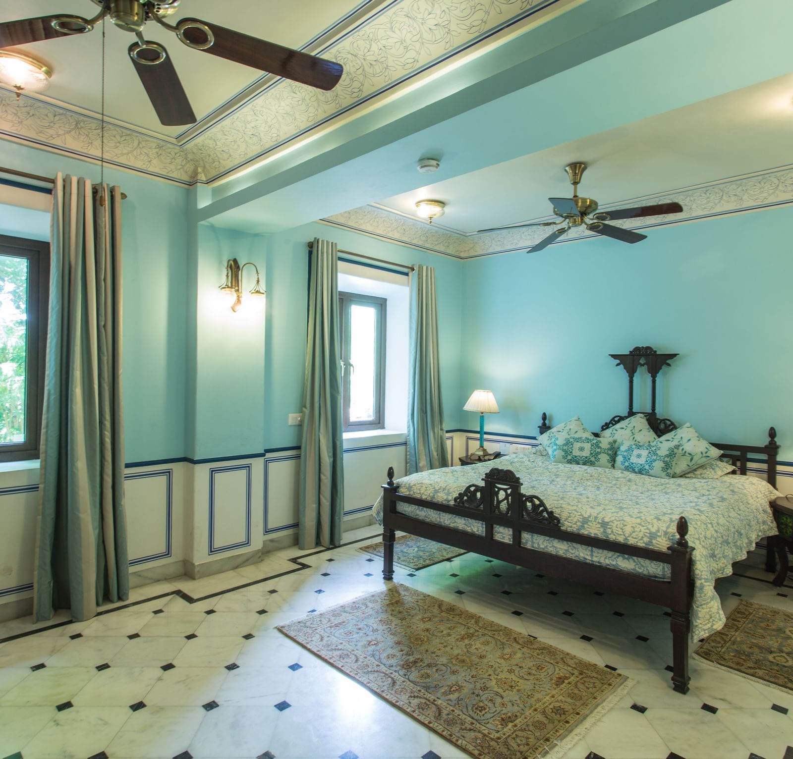 A spacious bedroom at Royal Heritage Haveli with a bed, seating area, ceiling fans, and light blue walls.