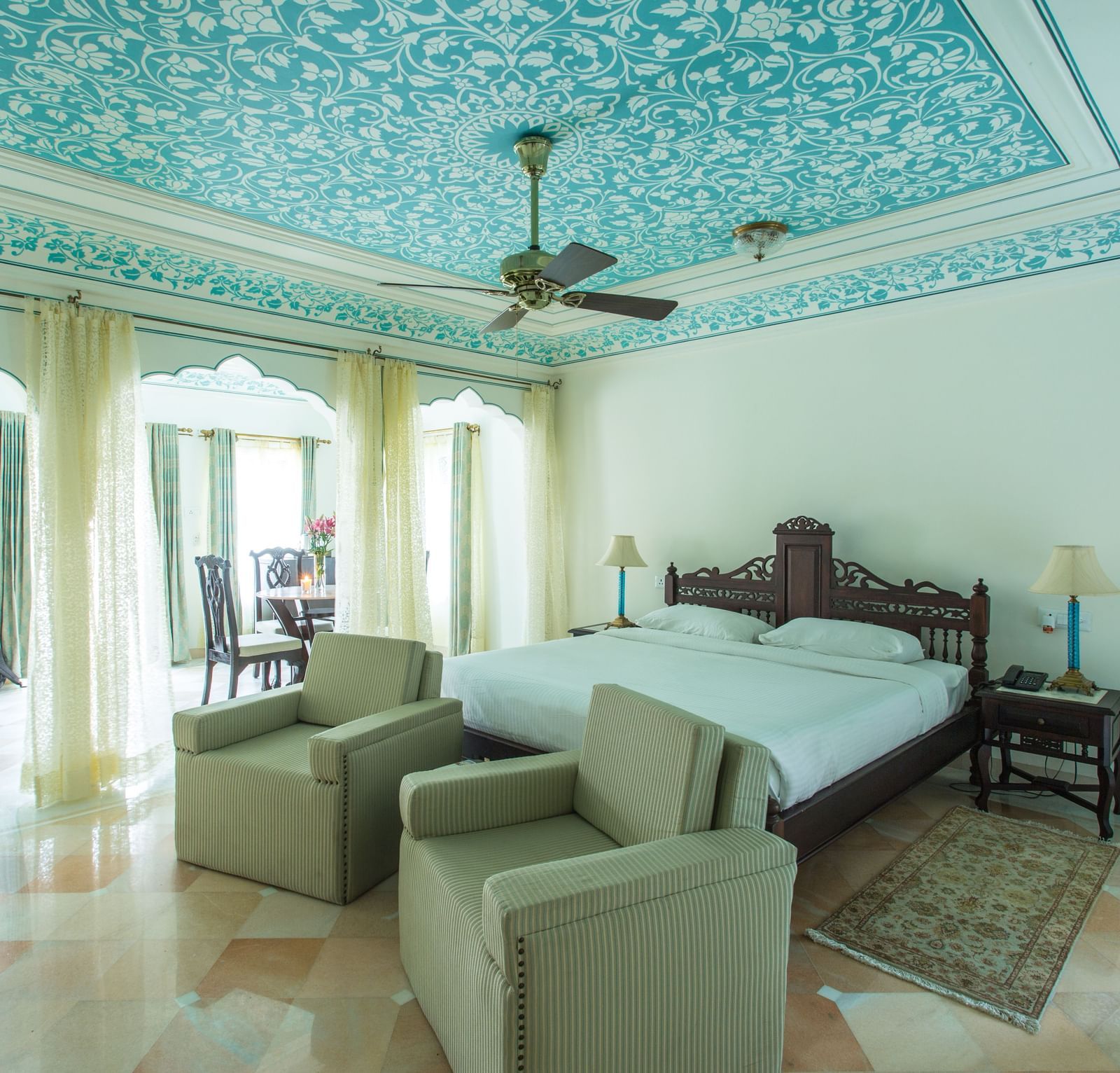 A spacious room at Royal Heritage Haveli with blue patterned ceilings, a seating area, and large windows.