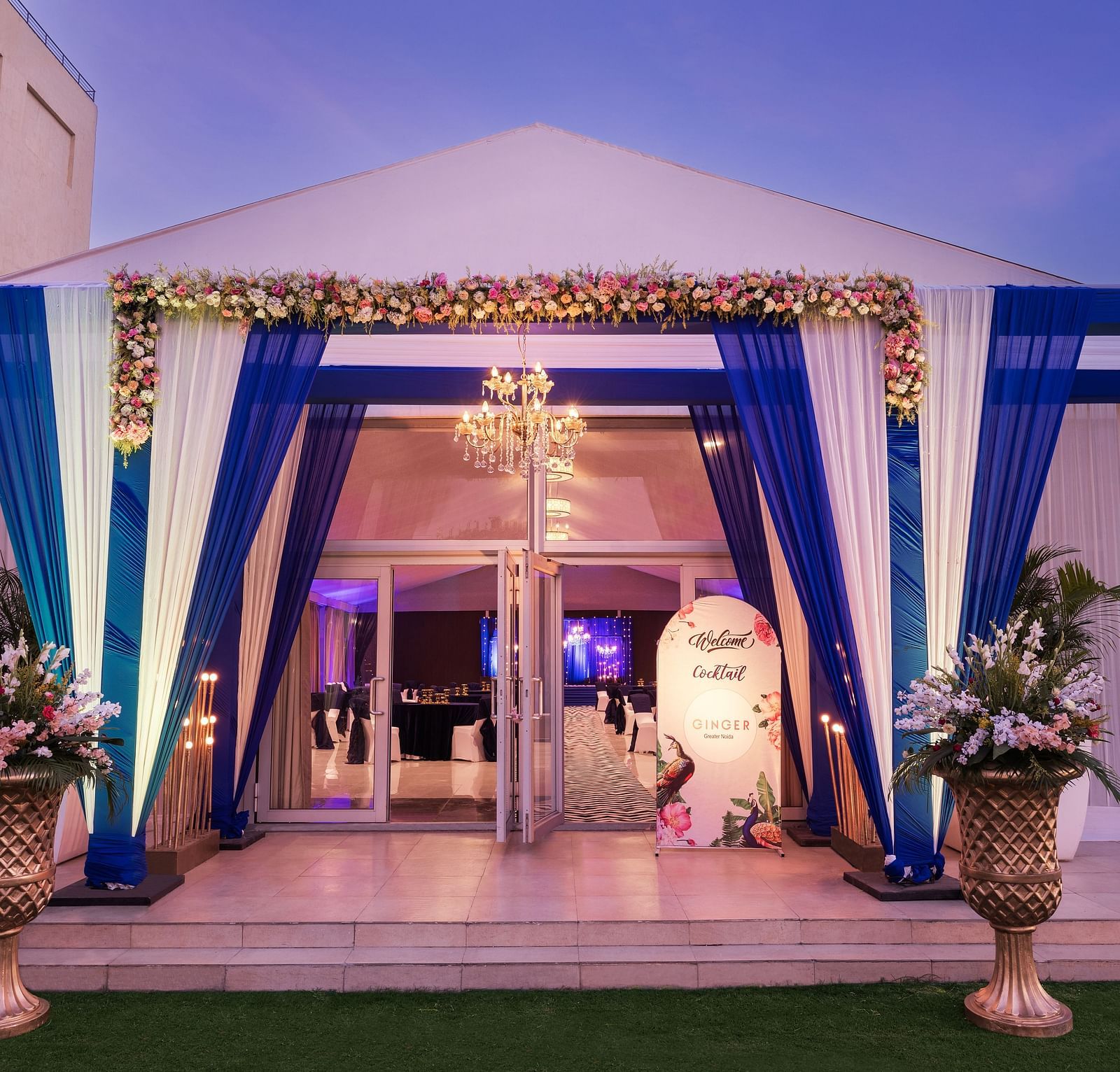 an entrance to a hall with a sign board beside the entry gate and blue and white curtains in front of the entrance - The Hideaway Banquets & Lawns, Greater Noida
