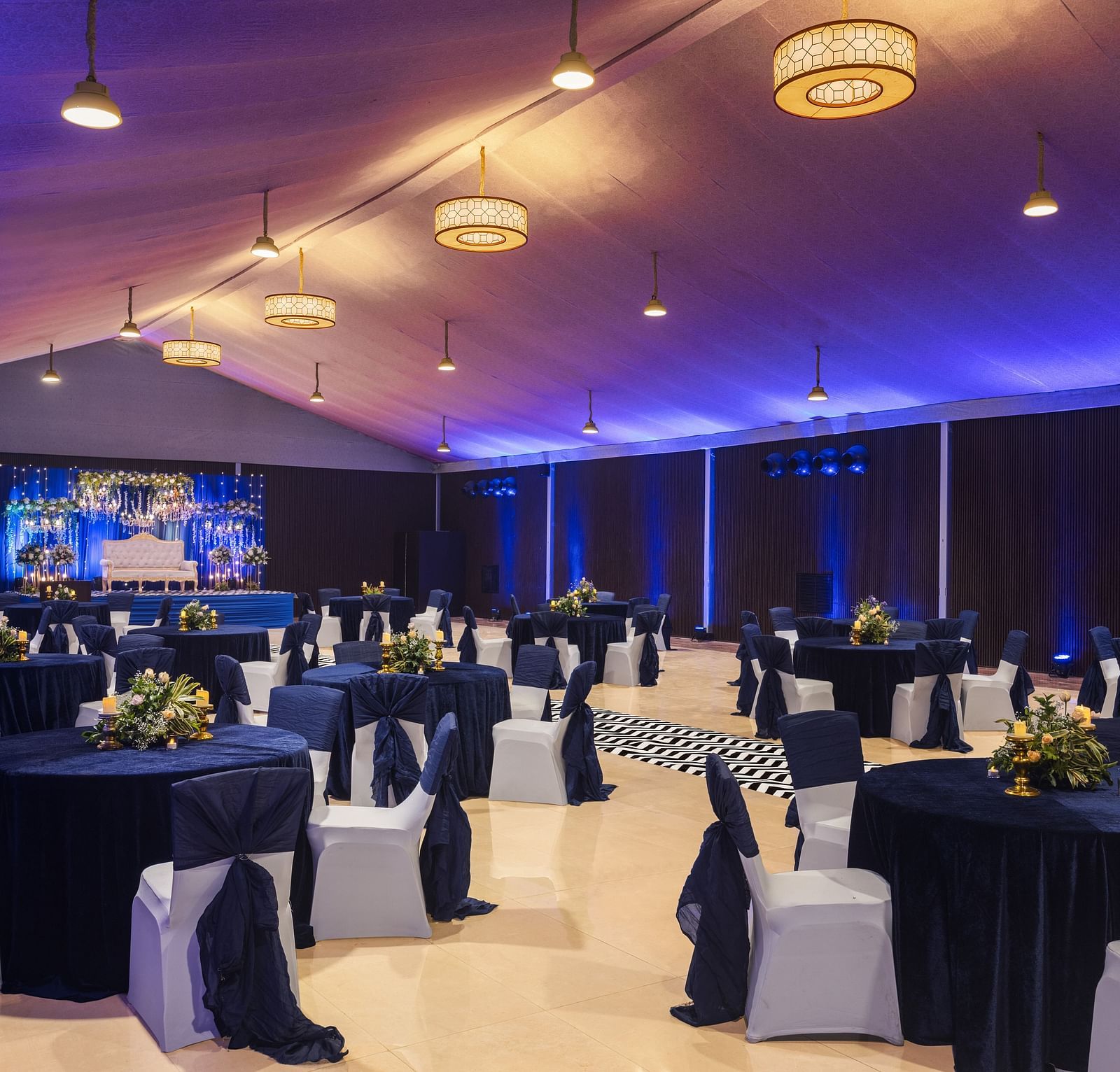 clusters of chairs and tables scattered across a room with chandeliers lighting up the hall - The Hideaway Banquets & Lawns, Greater Noida