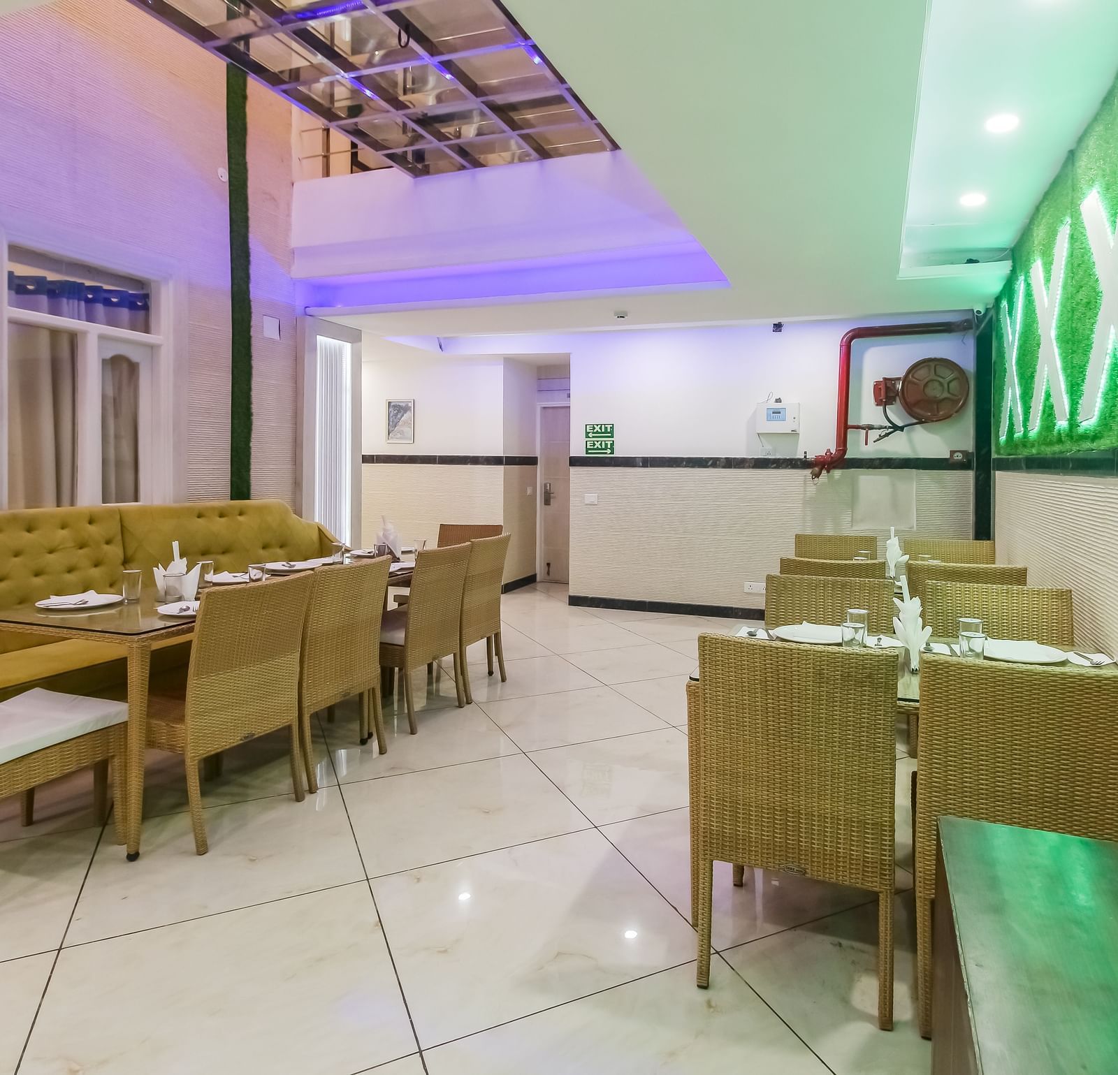 A restaurant interior with a long tufted sofa, wooden tables and chairs, a decorative wall design, and a tiled floor, lit by soft lighting. - Hotel Diamond Plaza, Chandigarh.