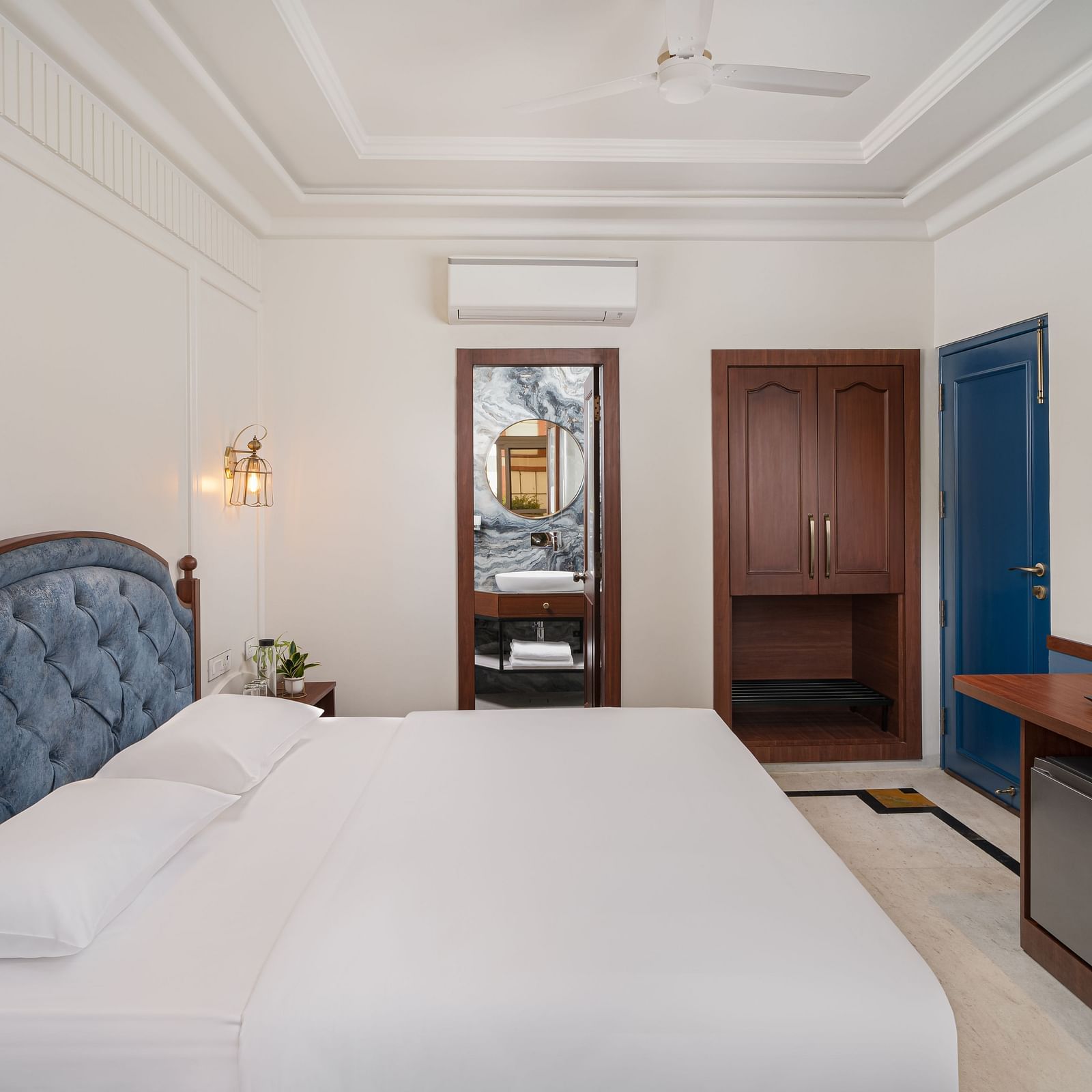 A side view of the room features a spacious bed, a wall-mounted television directly opposite the bed, and wooden furniture | Hotel Ganga Maiya