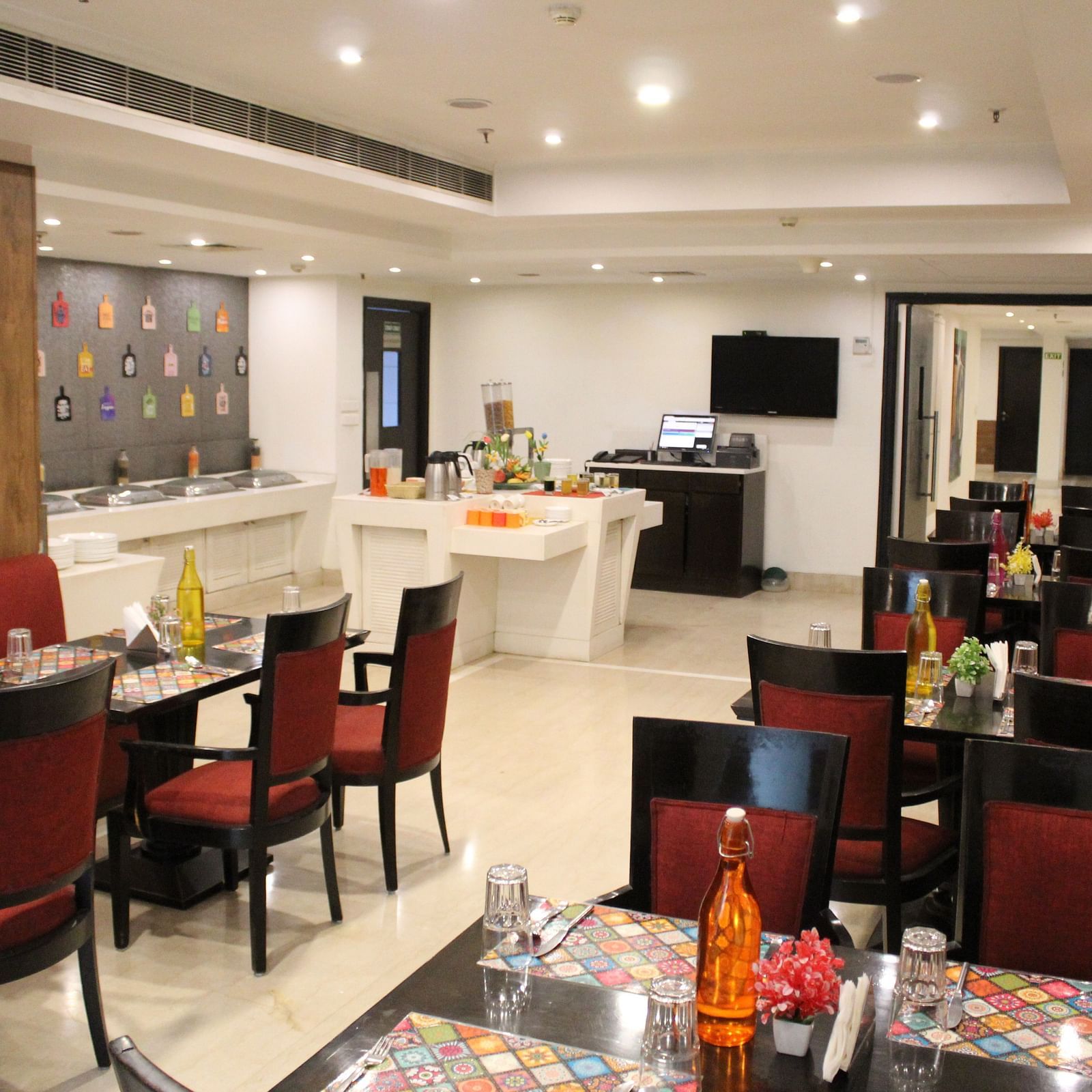 An image of a restaurant several sets of chairs and table where plates, cutlery, napkin, water bottles and other items are kept - Inde Hotels Vista Woods