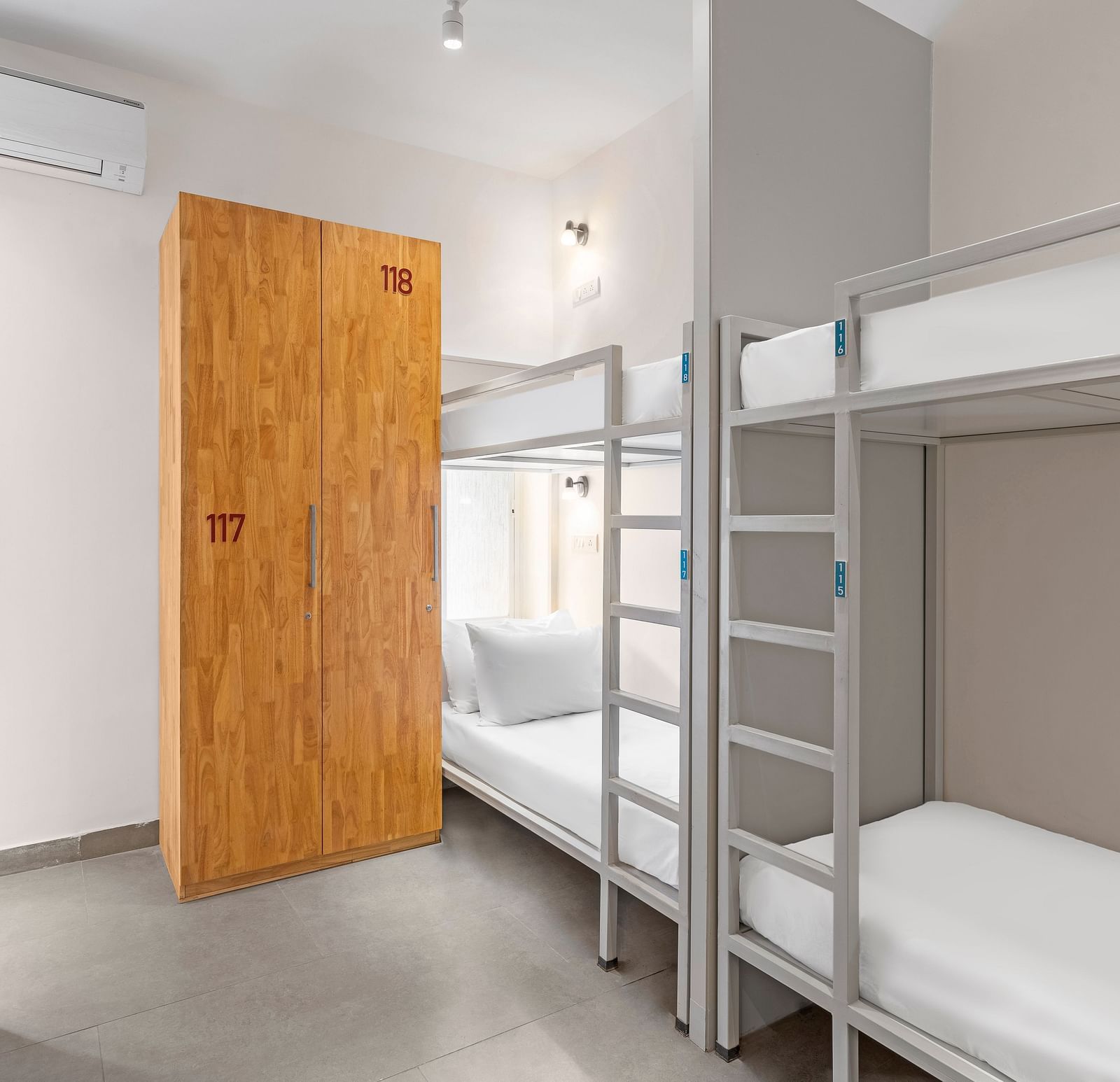Dorms at Bedzzz in Varanasi feature a practical layout with built-in cupboards and a door, ensuring privacy and ample storage space. The design creates a comfortable environment for guests, making it an ideal choice for travelers seeking a cozy stay.