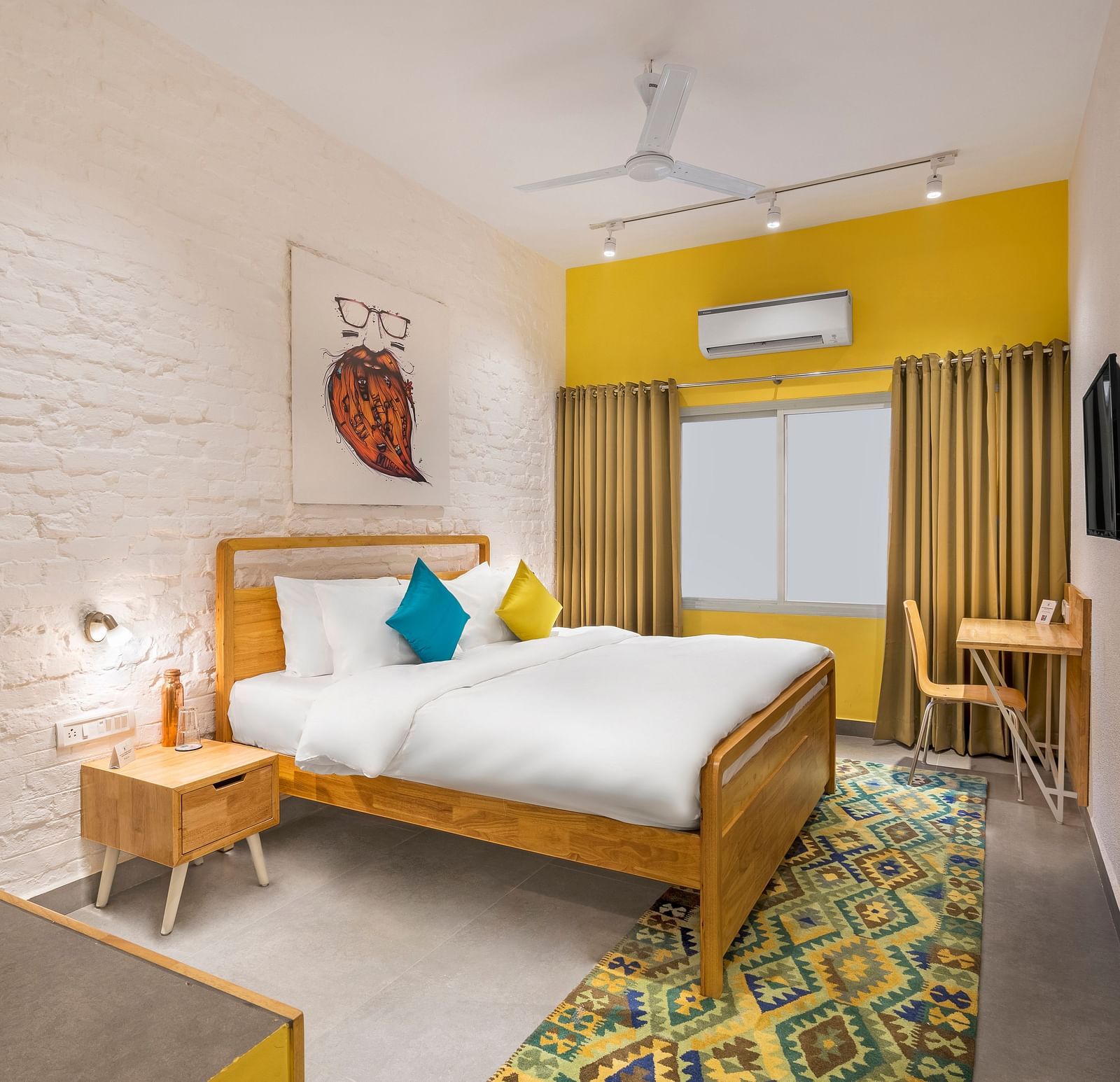 An interior image of the standard room at Bedzzz Varanasi showcases a spacious layout, featuring a comfortable double bed, a cozy floor mat, a stylish study table and chair, a charming coffee table, elegant curtains, an air conditioner for a refreshing amb