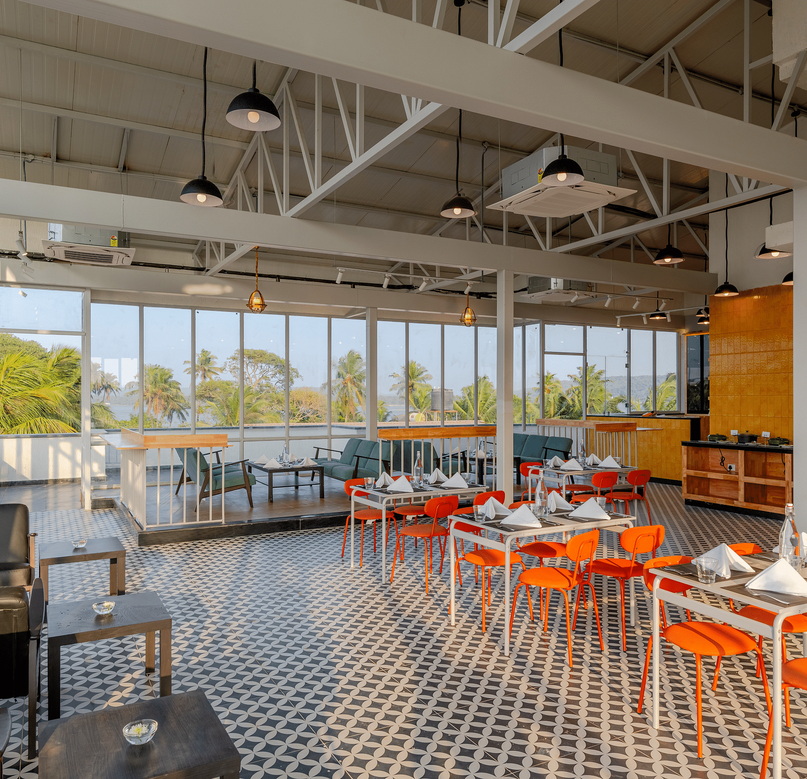  spacious and airy restaurant with industrial-style exposed ceiling, large windows letting in natural light, and a color palette of orange and grey, providing a relaxed dining atmosphere  at Bedzzz Xclusiv Morjim, Goa