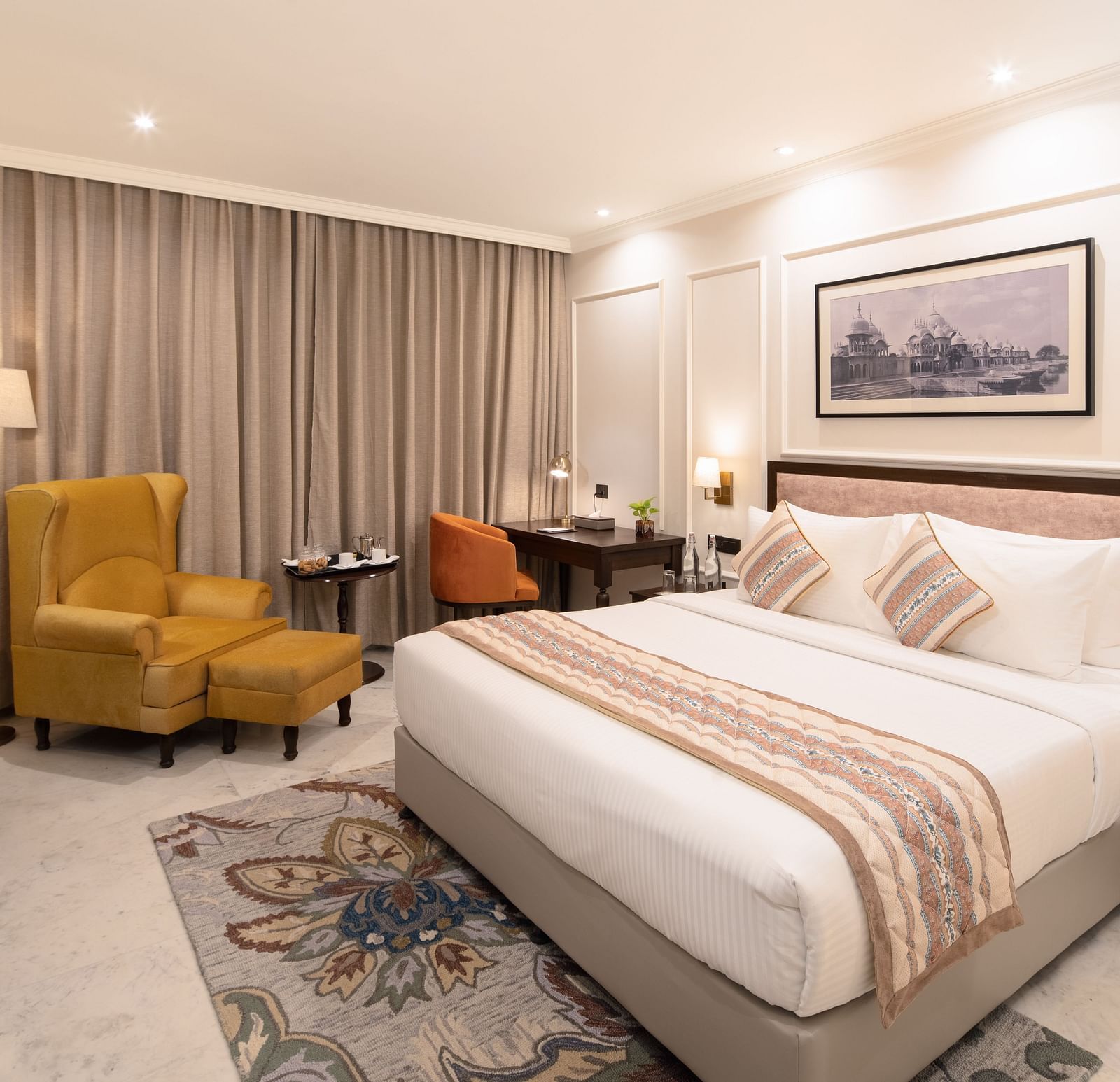 An image of a bedroom with bedside table, photo frame hanged on the wall, work desk with sofa chair, and a flat TV screen - Brij Eternity, Vrindavan
