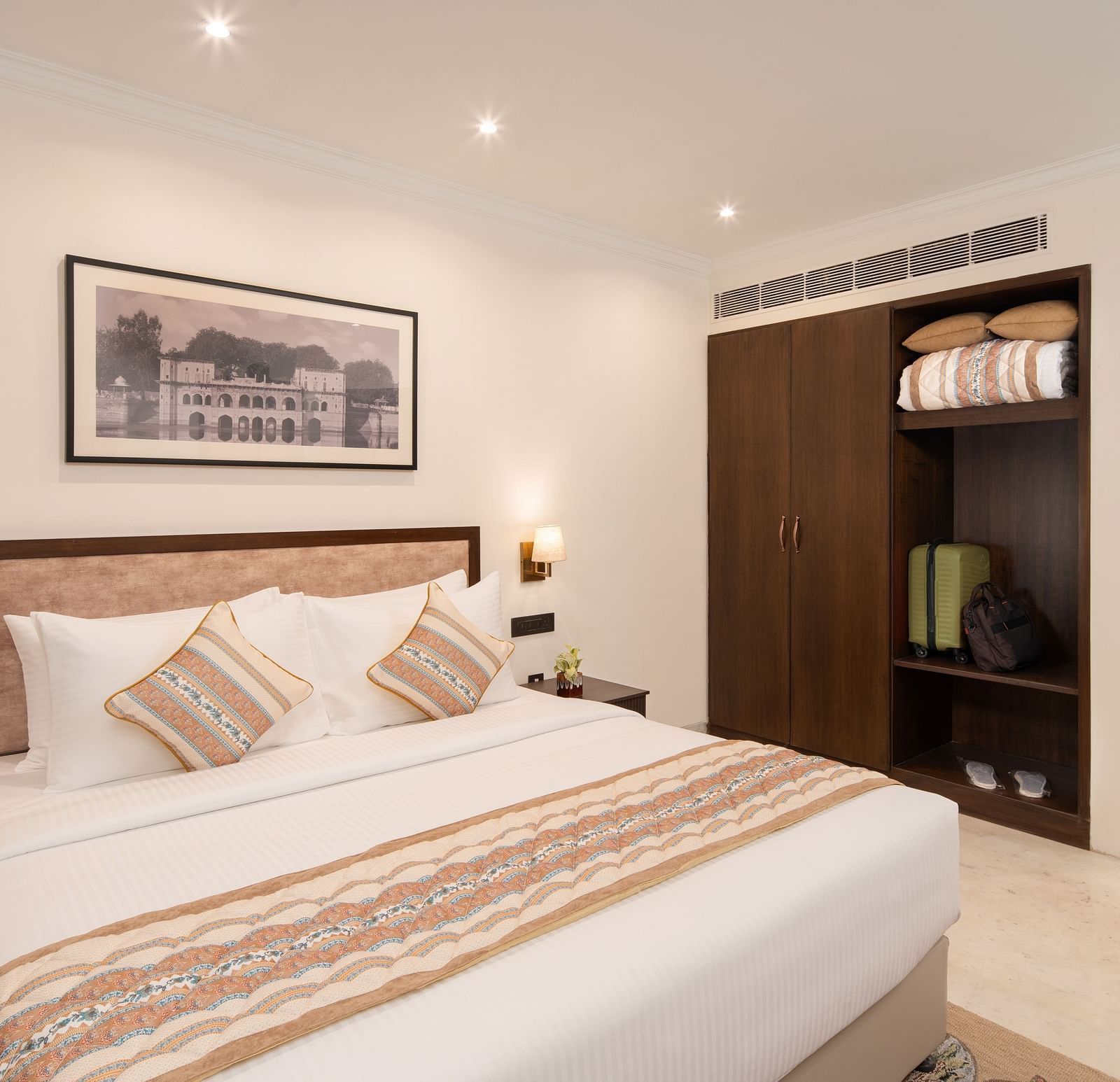 An image of a bedroom with bedside table, photo frame hanged on the wall, work desk with sofa chair, a flat TV screen, and a wardrobe - Brij Eternity, Vrindavan