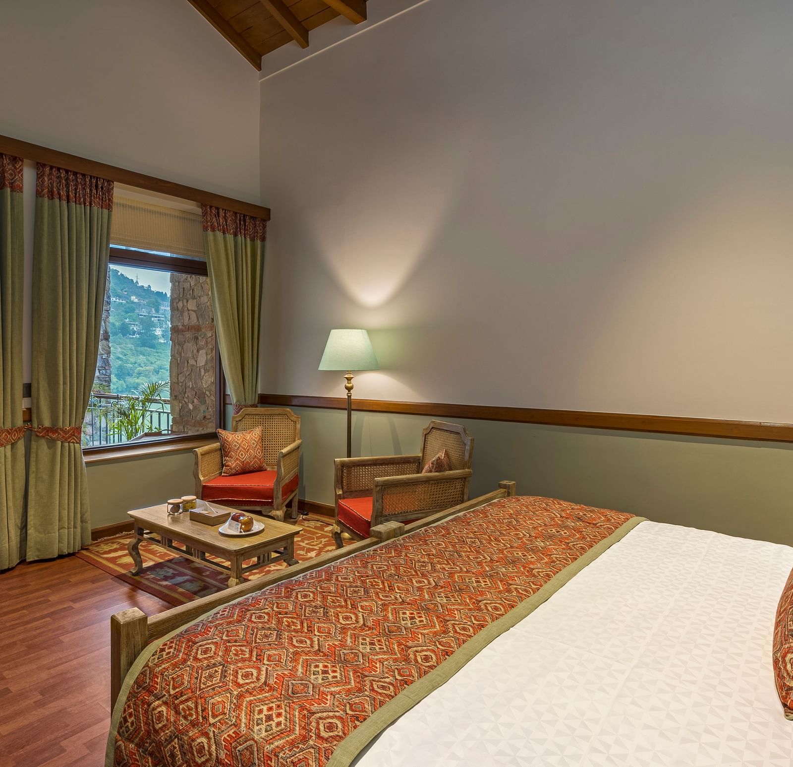 Top head view of Superior Rooms showcasing a cosy, royal interior with a comfortable bed, chair, and table, complemented by a beautiful hill view.