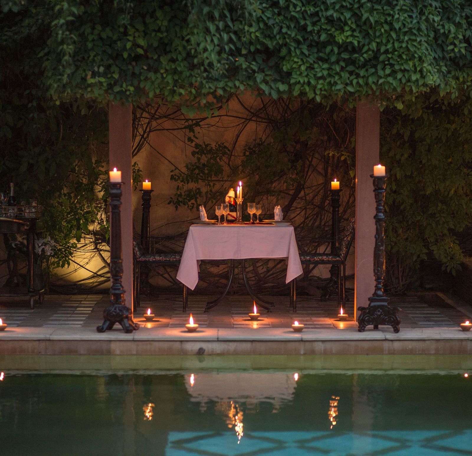 A beautifully lit outdoor setup with candles and a table next to a water feature, possibly at Royal Heritage Haveli.