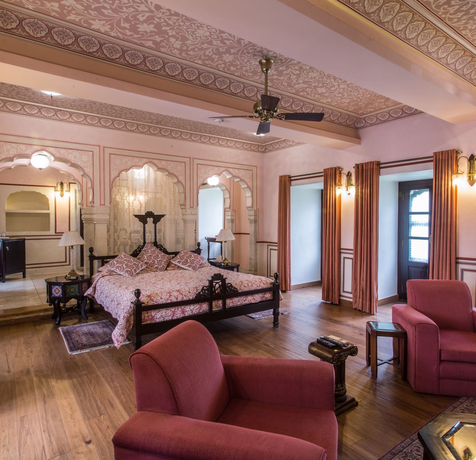 A spacious living area of a suite at Royal Heritage Haveli with traditional furniture, a ceiling fan, and light-coloured walls.