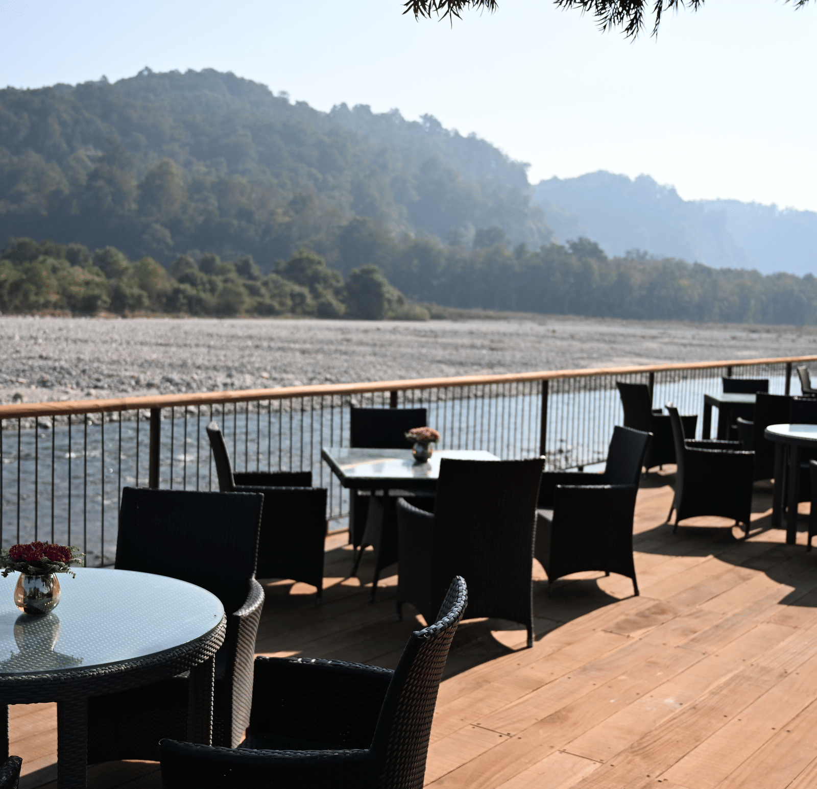 A wide shot of an empty outdoor dining terrace with tables and chairs next to a large river, under a overcast sky at The Corbett Hideaway.