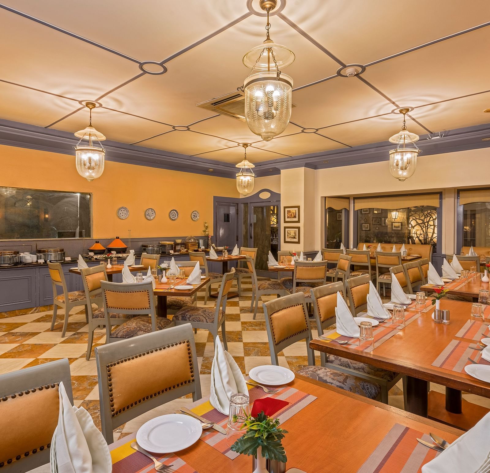 a view of a restaurant with a buffet setting and clusters of tables and chairs with lighting from four chandeliers - The Manor, Kashipur