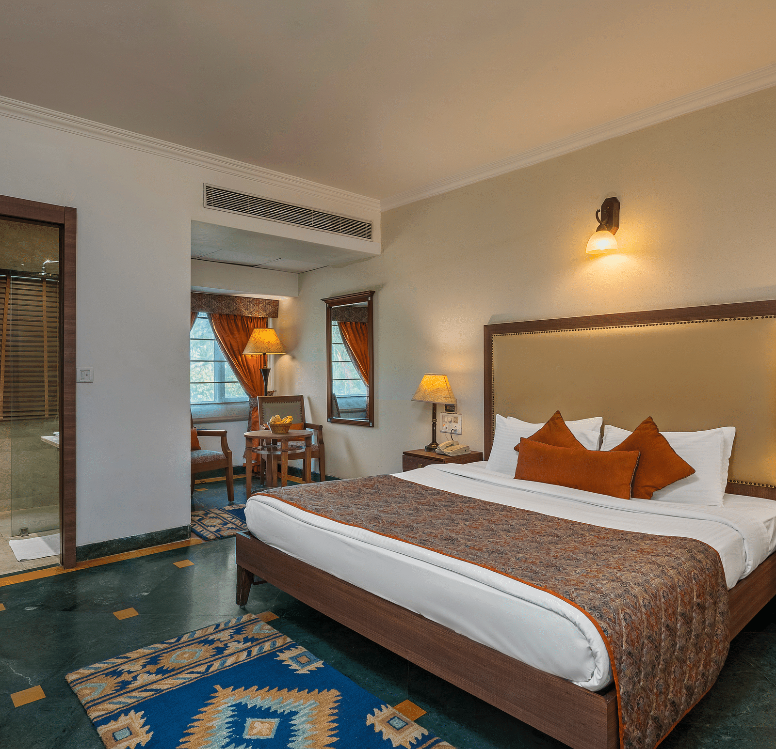 A bedroom with a large bed with side drawers placed on both sides of the bed, with an overhead lamp and side lamps - The Manor, Kashipur