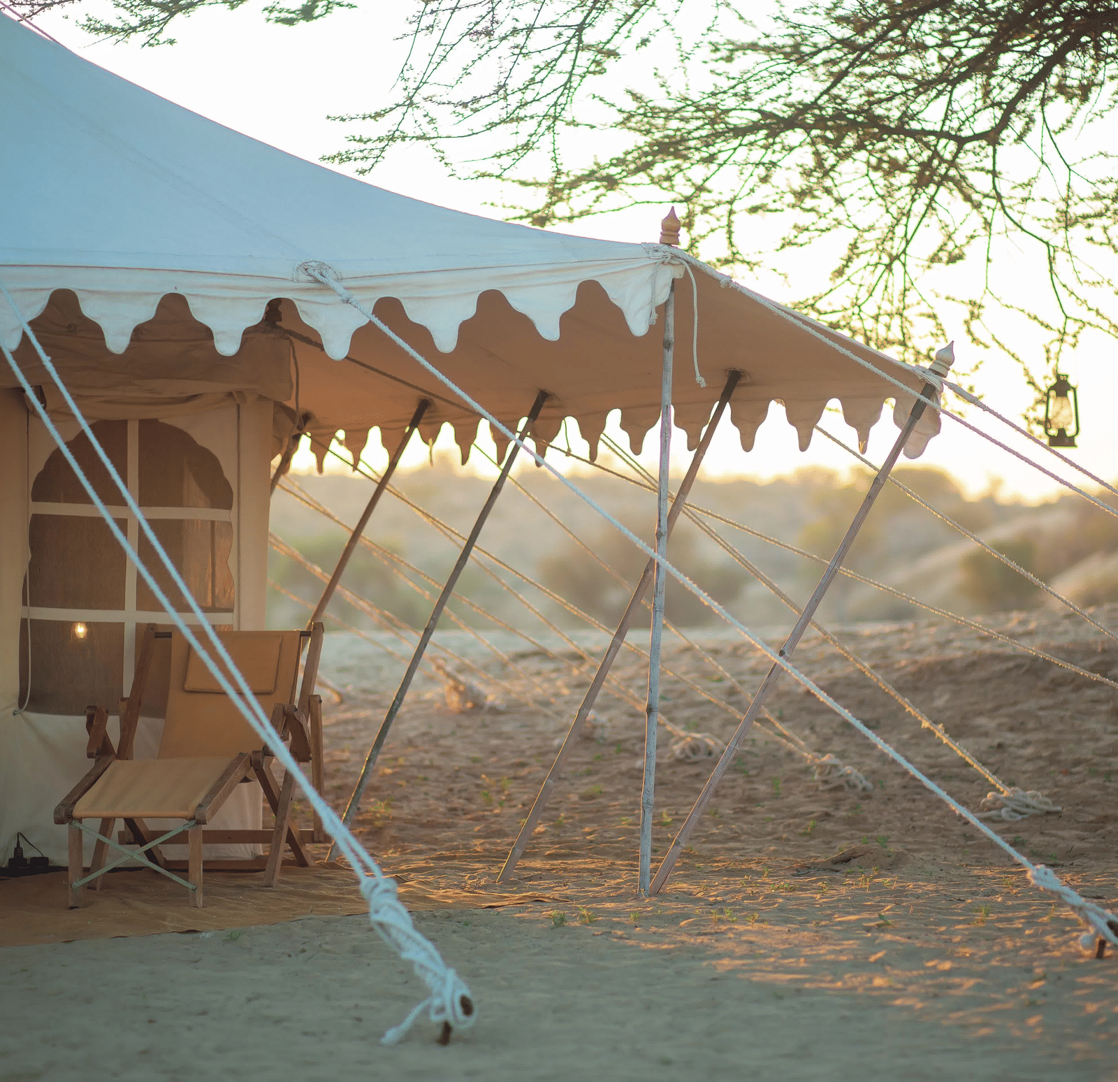 A luxurious white canvas safari tent is set up in the Thar Desert in Rajasthan, India, at sunset.