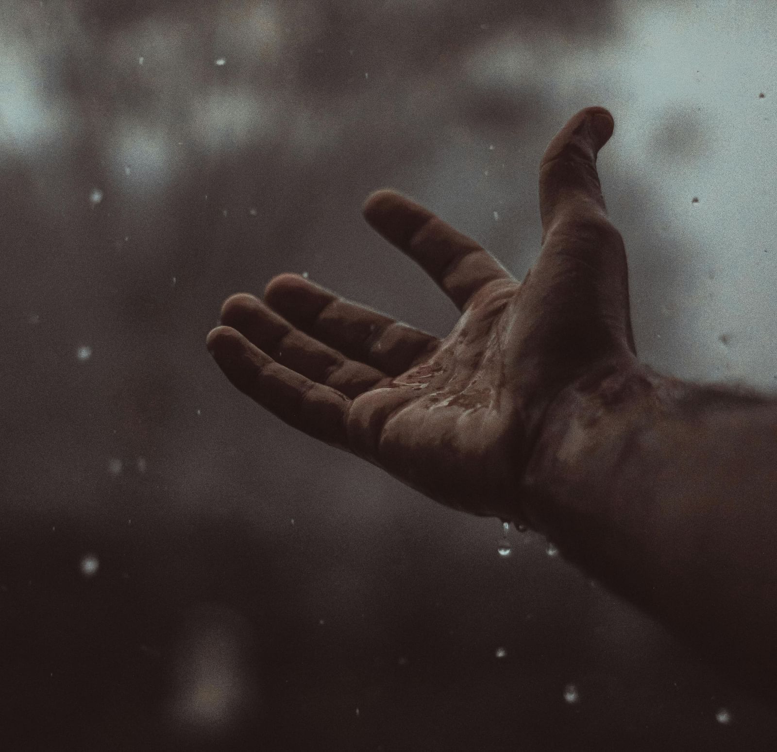 A hand is outstretched to catch raindrops, with a blurred background.