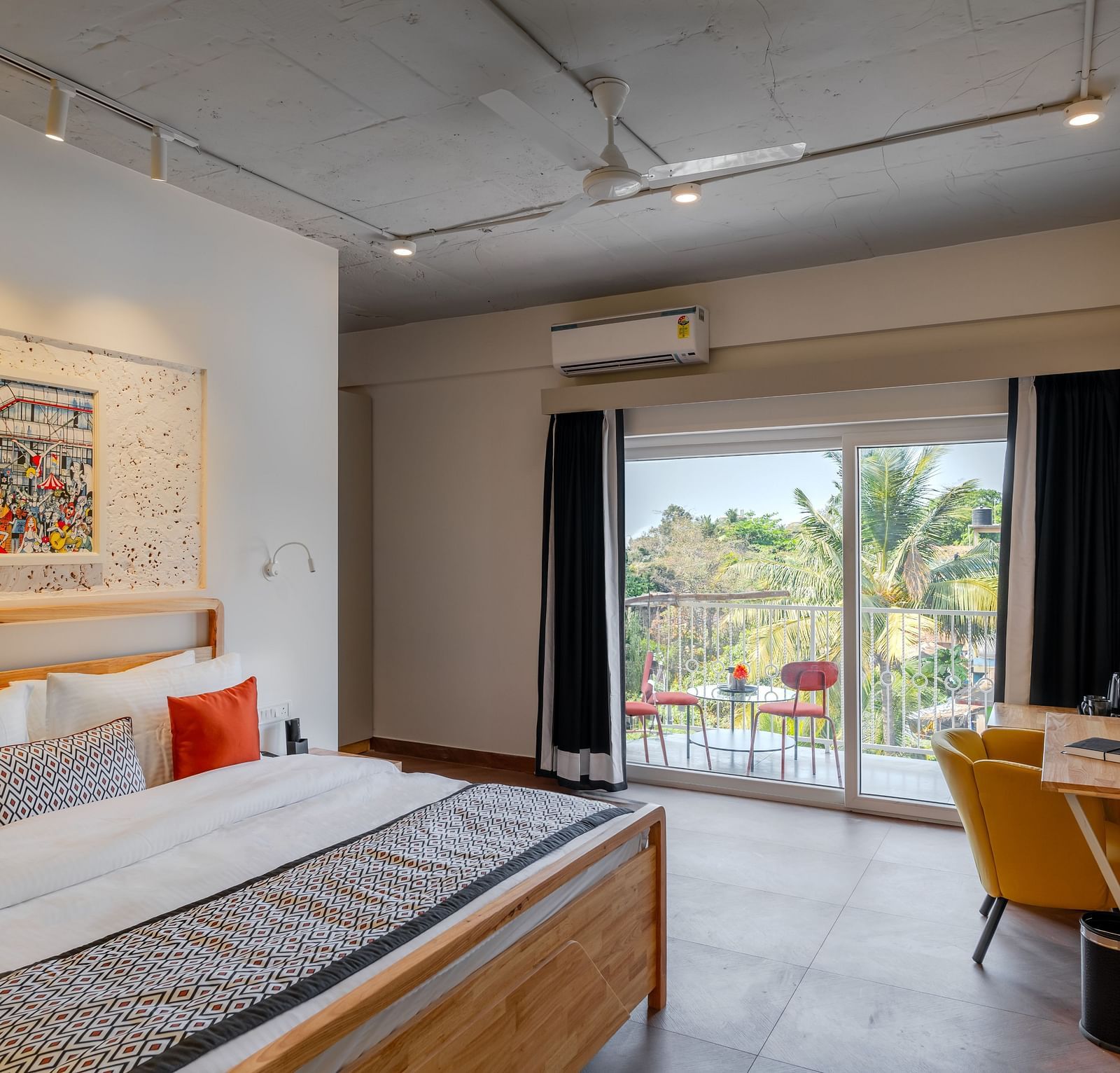 Bright hotel room with, flat TV screen, work desk and chair, vibrant art on the wall, and an access to the balcony at Bedzzz Xclusiv Morjim, Goa
