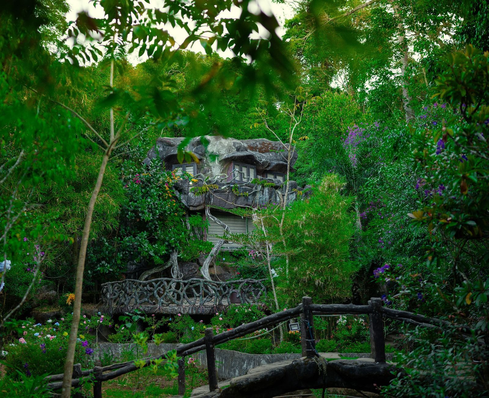 An image of a facade set amidst the forest and there's also a bamboo bridge  in front of the facade - Parakkat hotel & resorts