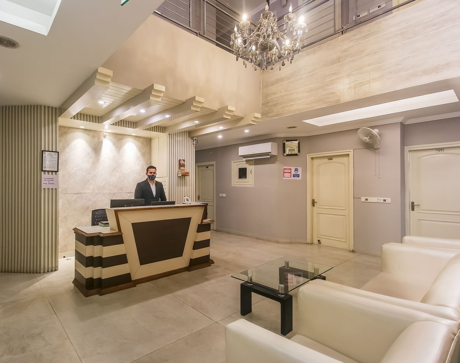 A hotel lobby with a reception desk, a chandelier, a seating area with white sofas, and a staff member behind the counter, lit by soft lighting. - Hotel Diamond Plaza, Chandigarh.