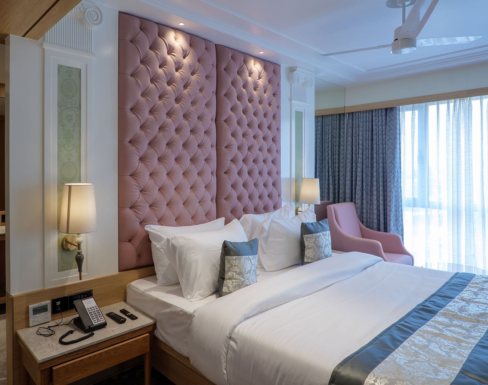 A room with a large bed featuring a pink tufted headboard, bedside tables, and an armchair with soft lighting - Melior Inn
